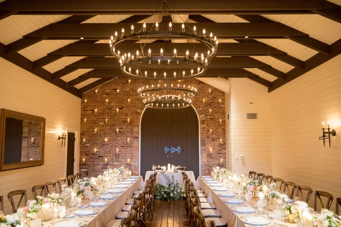 Elegant dining hall with long tables, candles, and chandeliers.