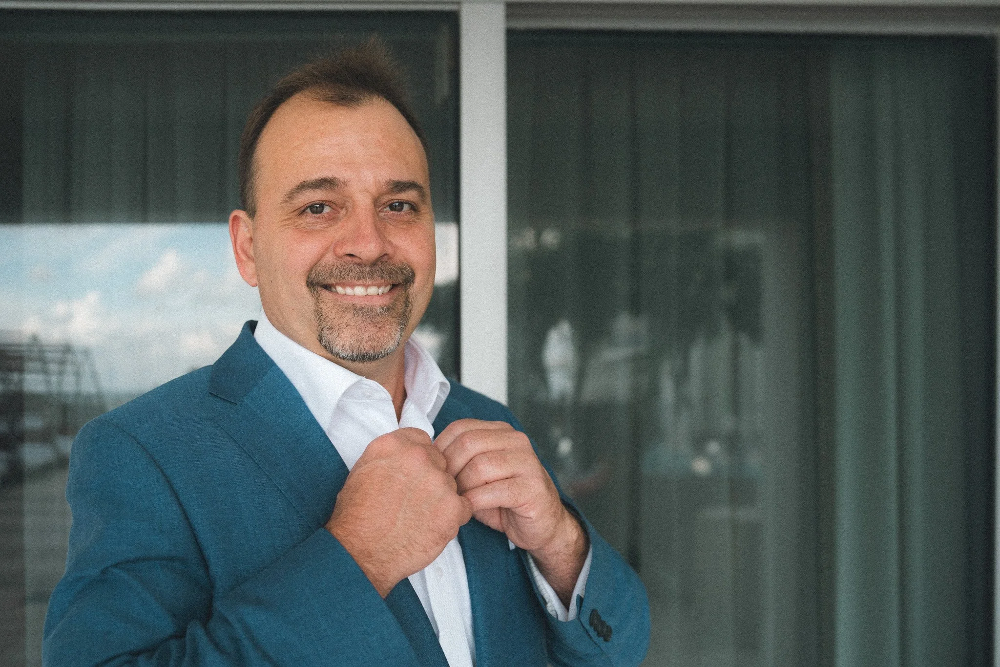 Man in a blue suit adjusting his collar and smiling outdoors.