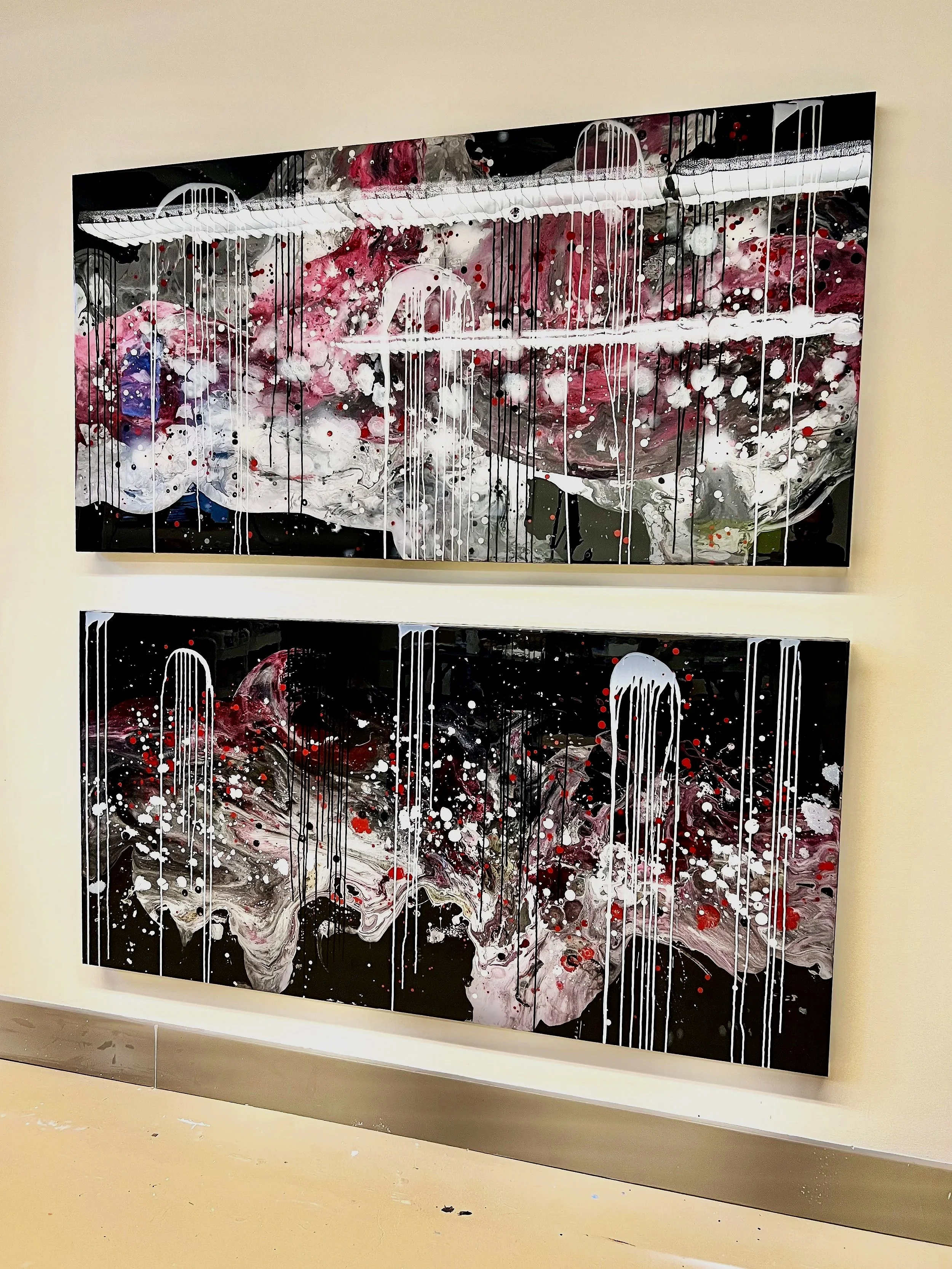 Two large abstract paintings with black, white, pink, and red splashes and drips, displayed on a white wall in an art gallery.