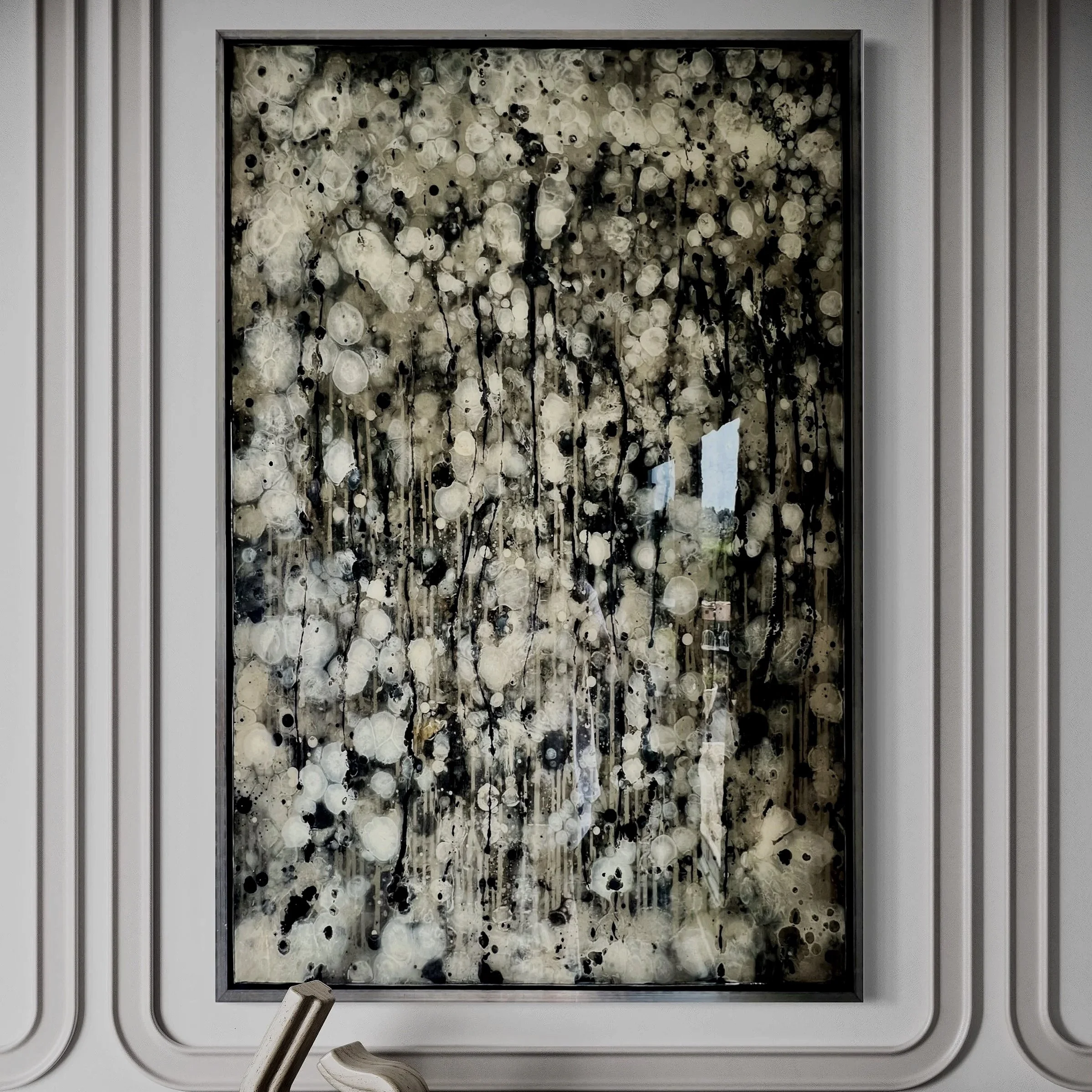 A photograph of an elevator door with an abstract black and white art piece above a modern black and gray console table. The art features a pattern of circles and drips, resembling an abstract splash of paint.