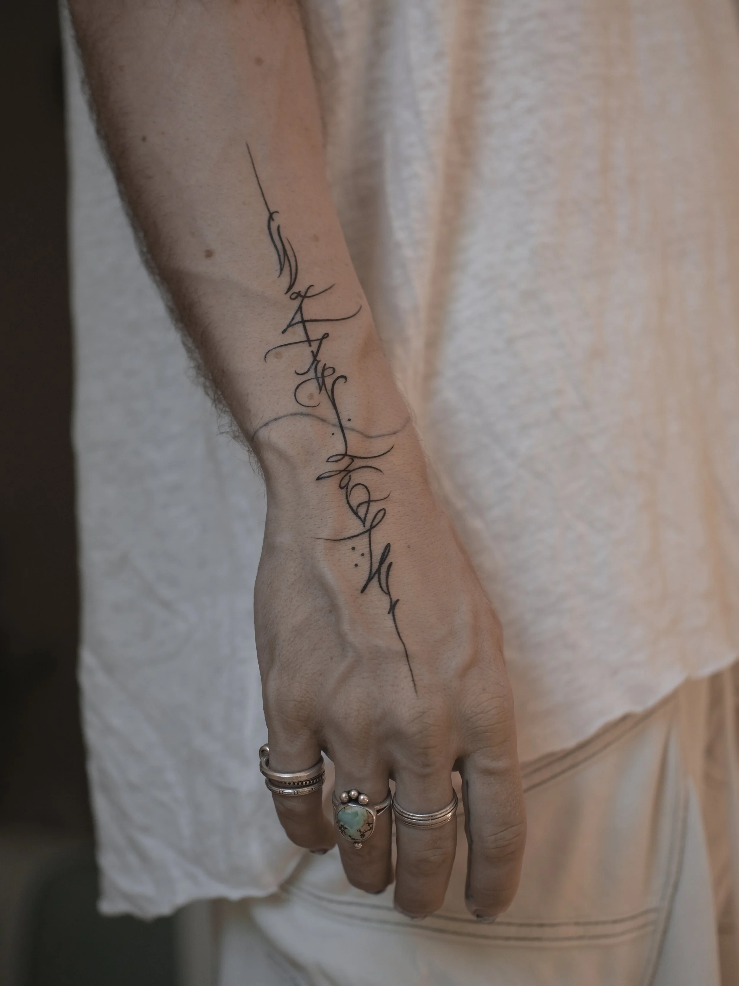Close-up of a person's hand showing multiple silver rings, and a tattoo on their forearm with elegant cursive writing.