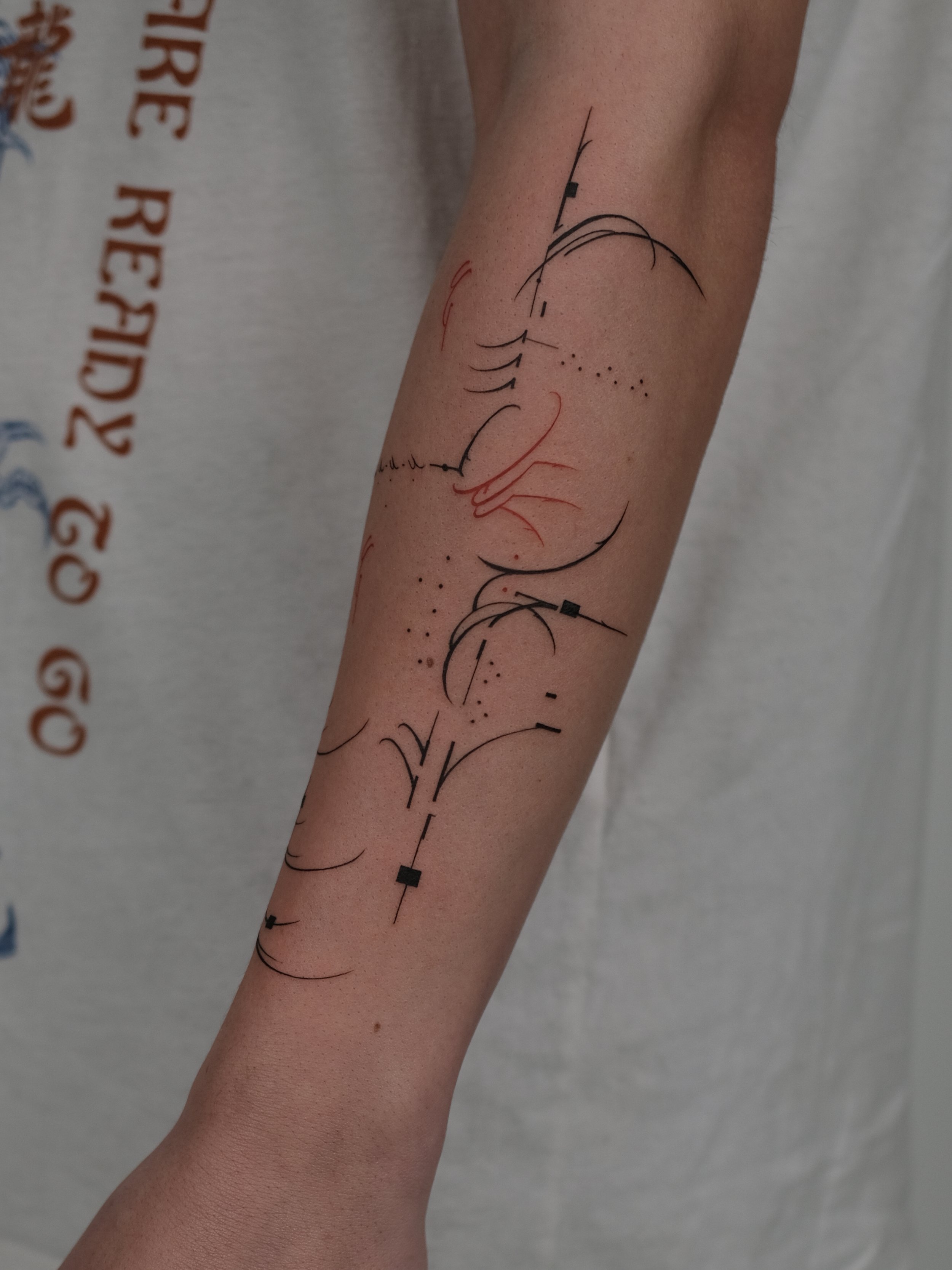 A person's arm with a colorful tattoo design that features abstract lines, curves, and geometric shapes in black and red ink.