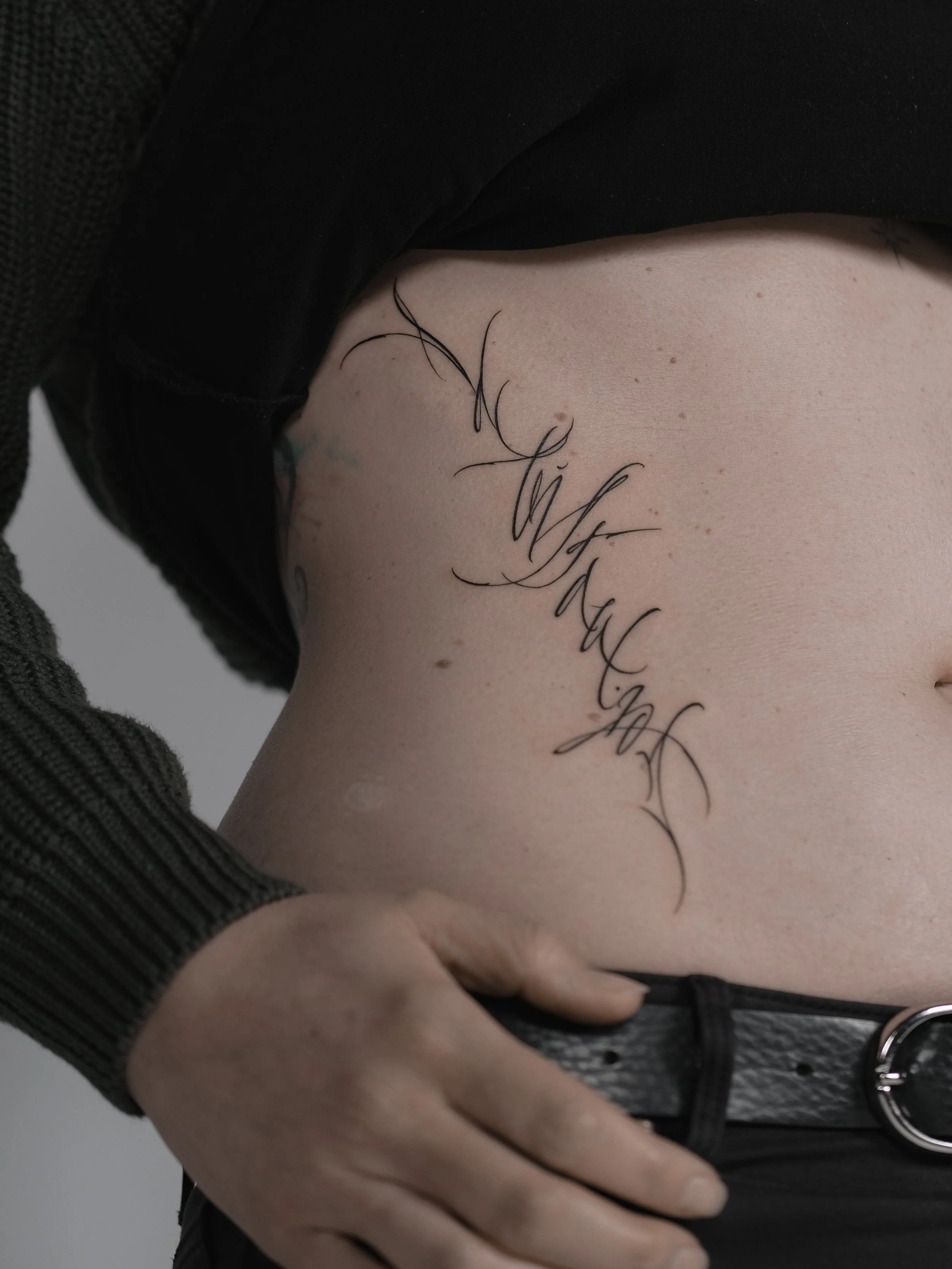 A person wearing black clothing with a tattoo on their side.