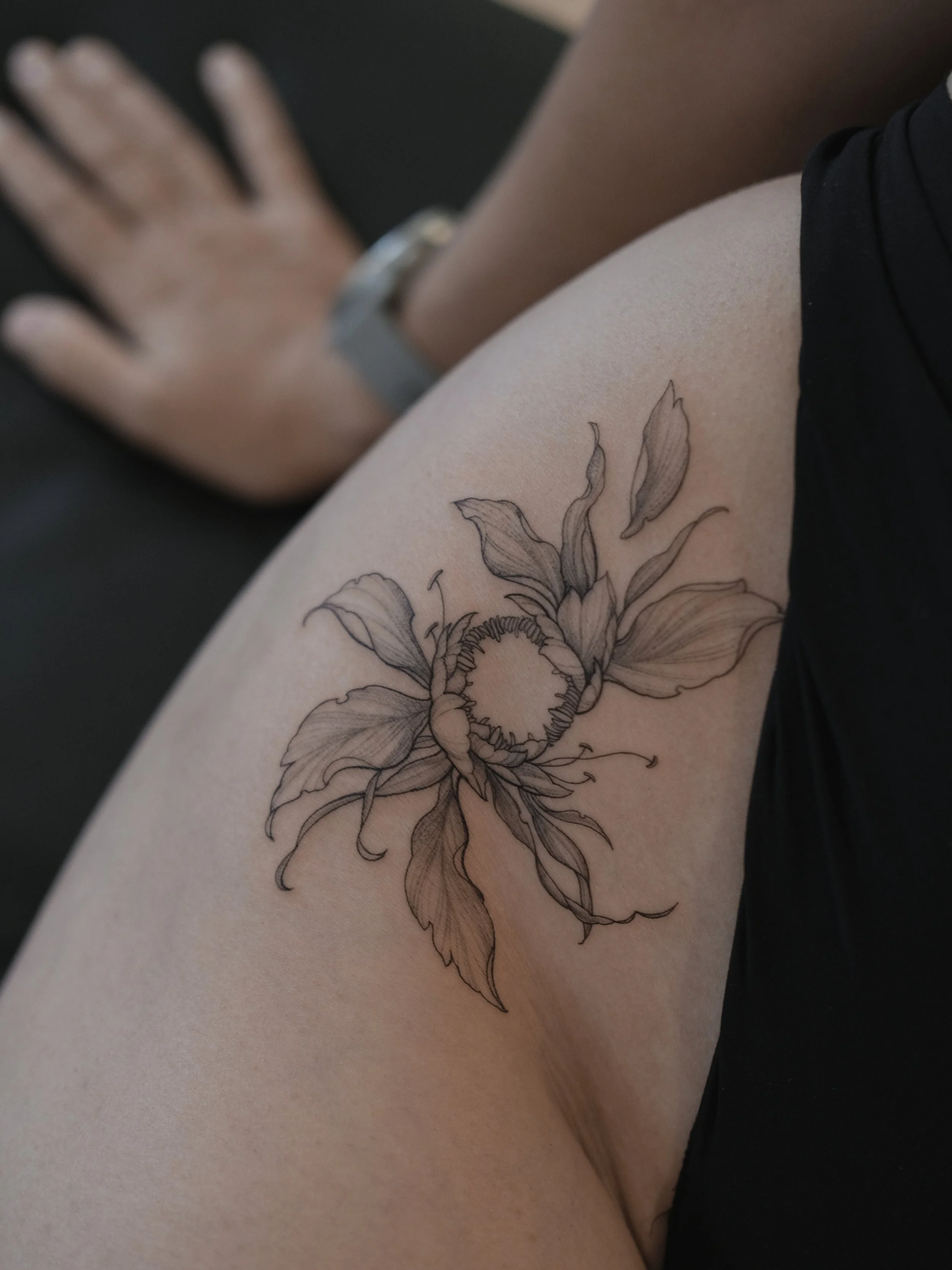 A person's thigh with a detailed floral tattoo and a wristwatch.