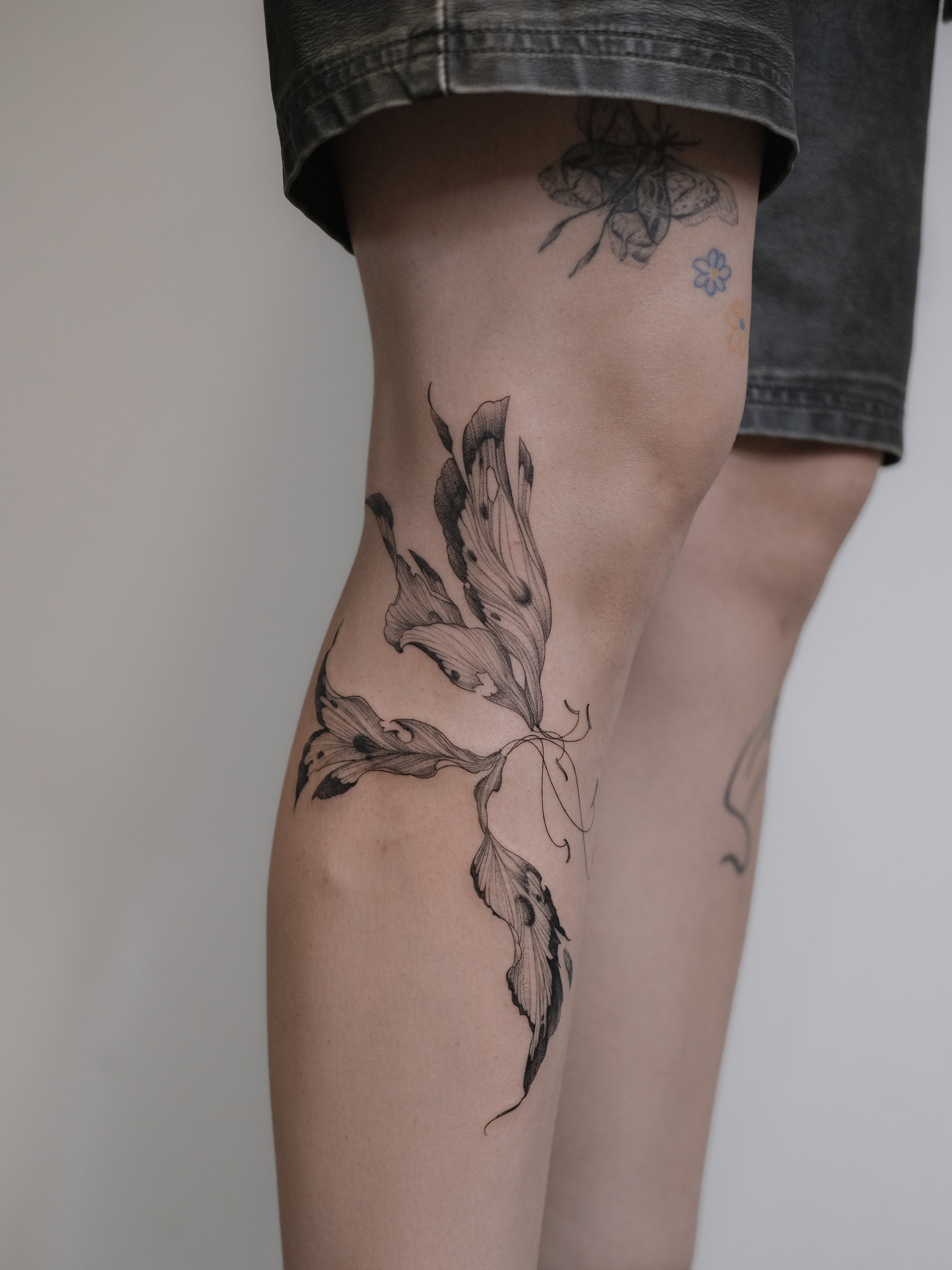 Close-up of a person's upper leg and thigh showing floral and butterfly tattoos on the skin.