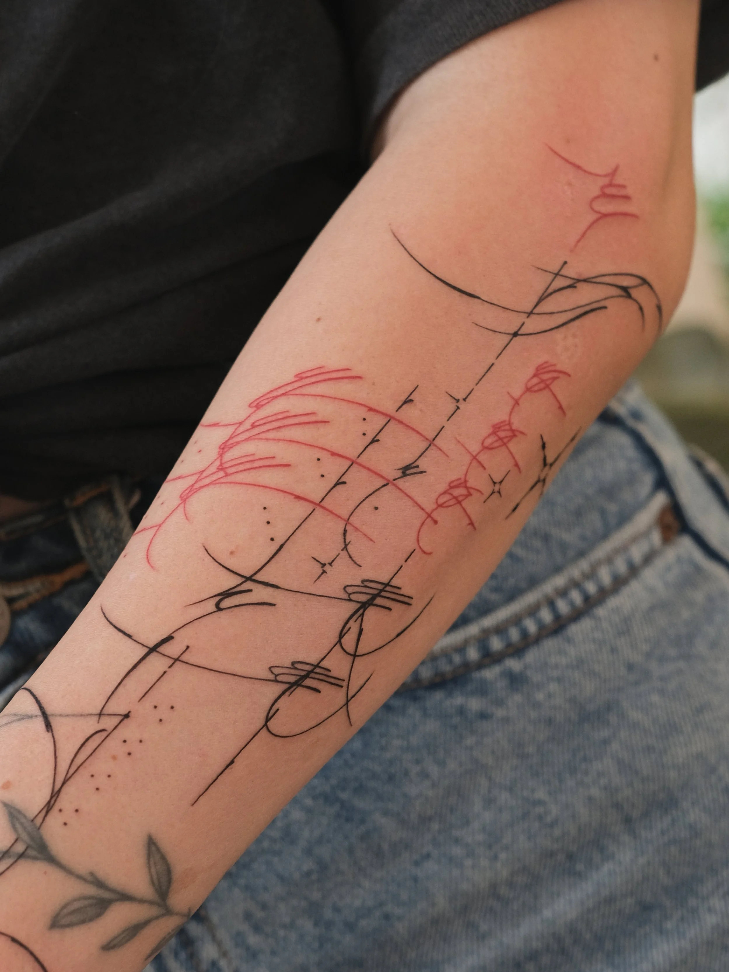 Close-up of a person's forearm with a colorful abstract tattoo design featuring black and red ink.