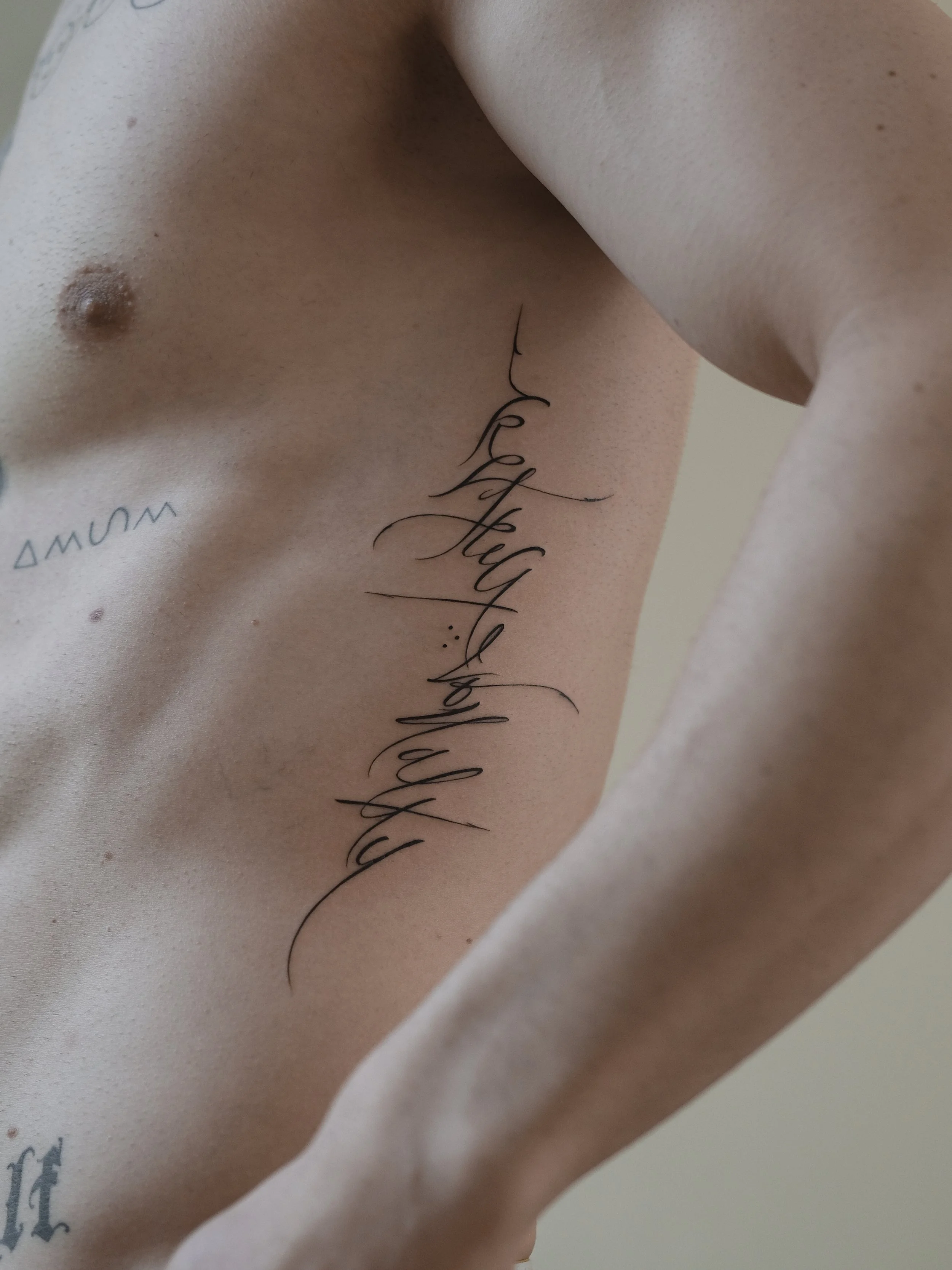 Close-up of a person’s upper torso with tattoos, including a cursive script that reads 'Love,' and skin with natural freckles and moles.