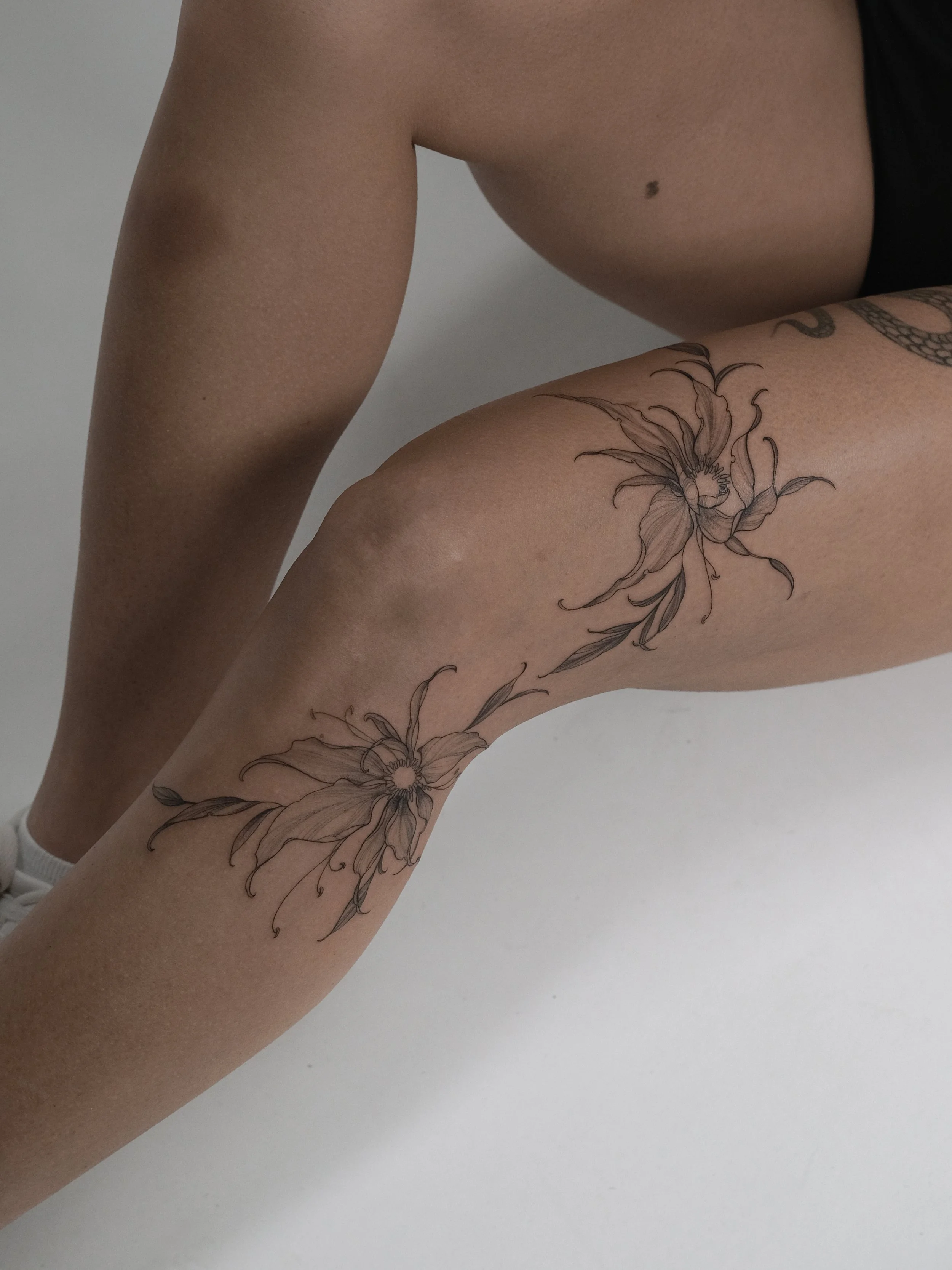 Close-up of a person's leg with a large floral tattoo, and part of the person's torso visible with a mole on the chest.