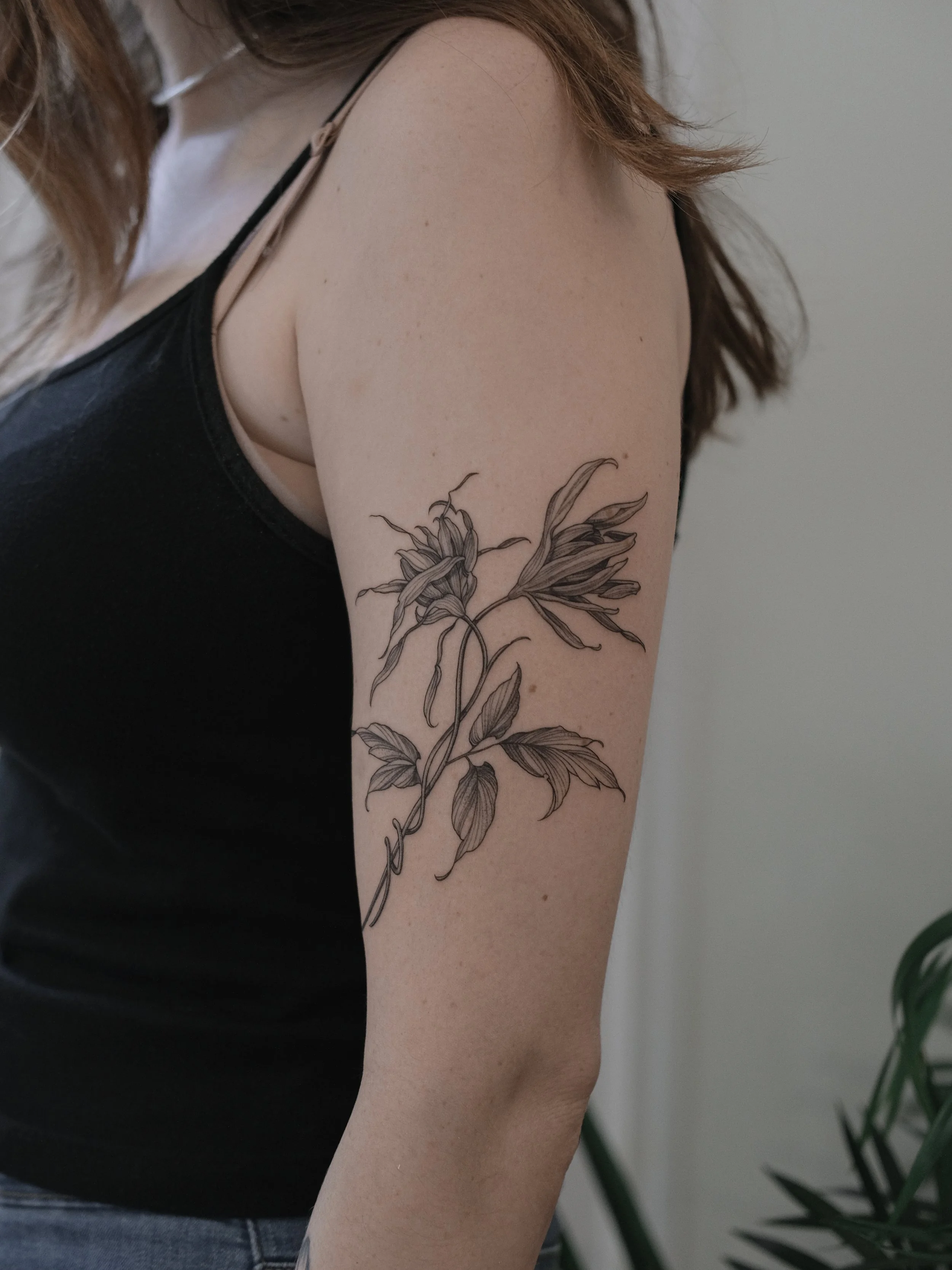 A tattoo of a floral design on a woman's upper arm, featuring detailed black and gray flowers and leaves.