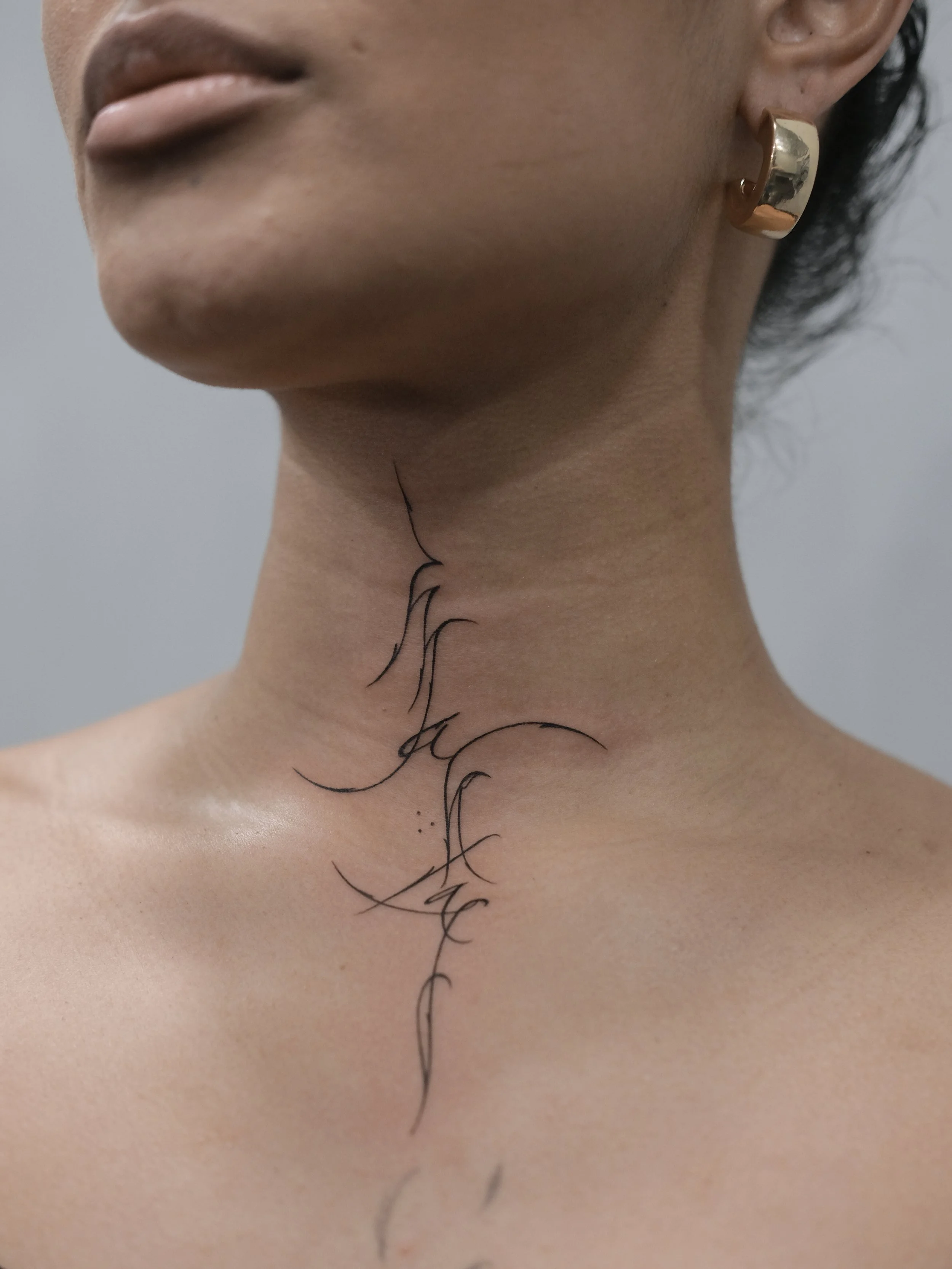 Close-up of a person's neck with black cursive tattoo and a gold earring.