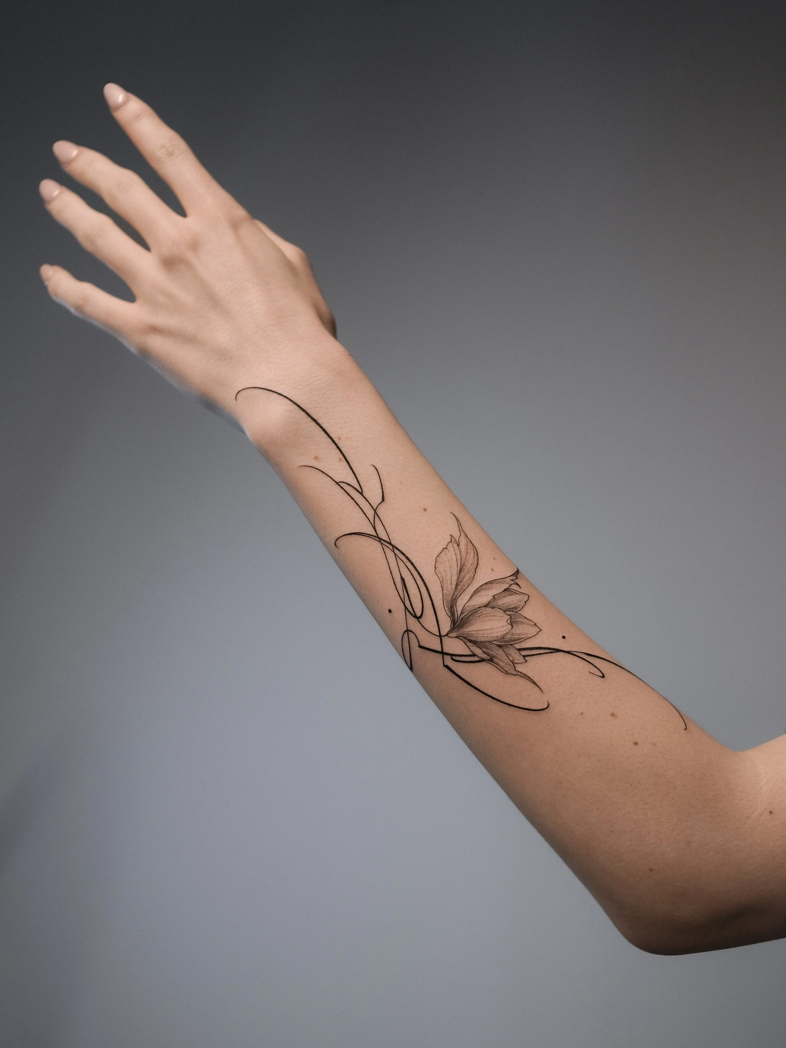 A person's arm with a floral tattoo on the forearm, extended against a plain dark background.