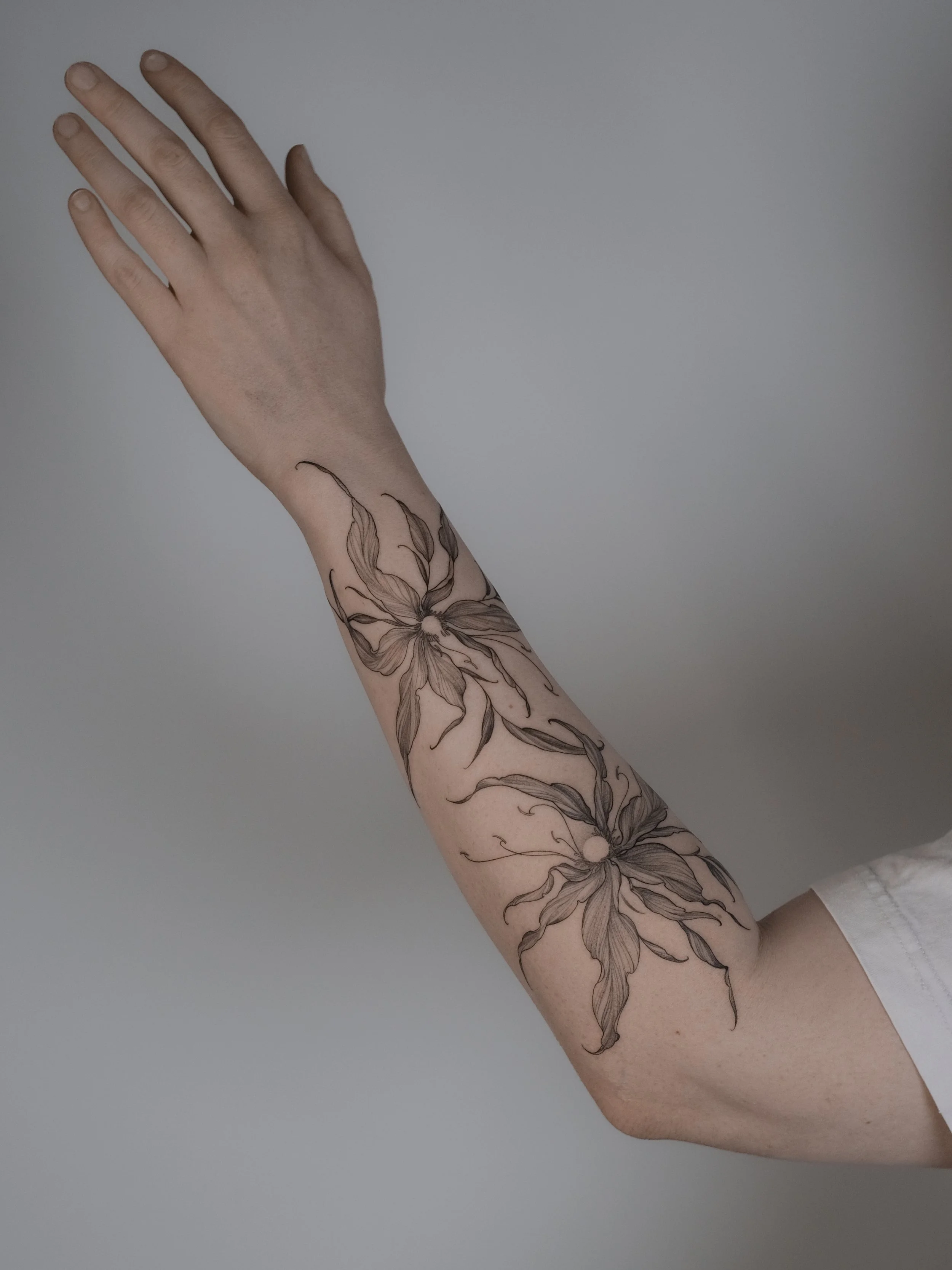 A person's arm with a tattoo of a flower and leaves extending from the wrist to the forearm.