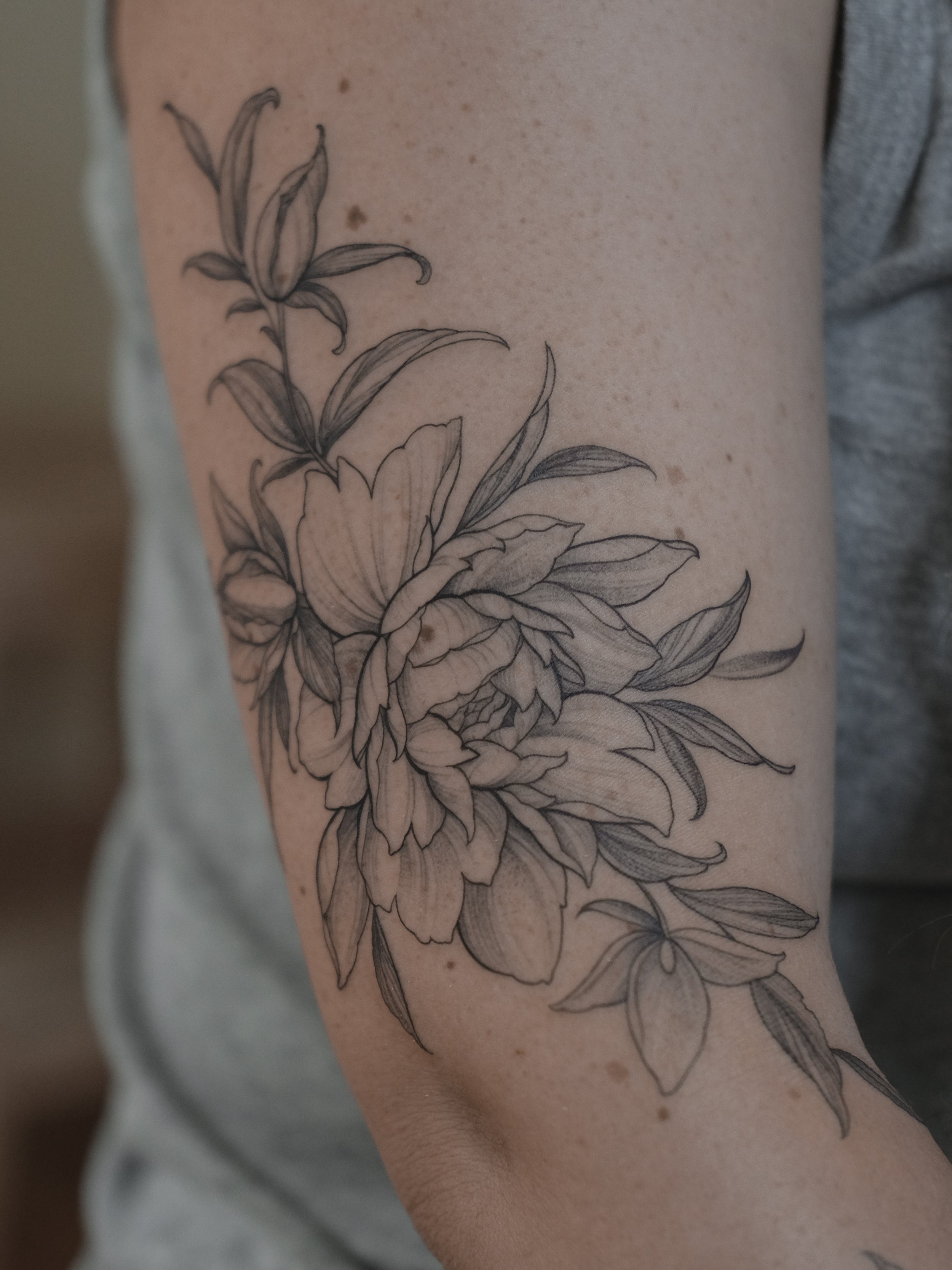 A black outline tattoo of a large, detailed flower with leaves on a person's arm.