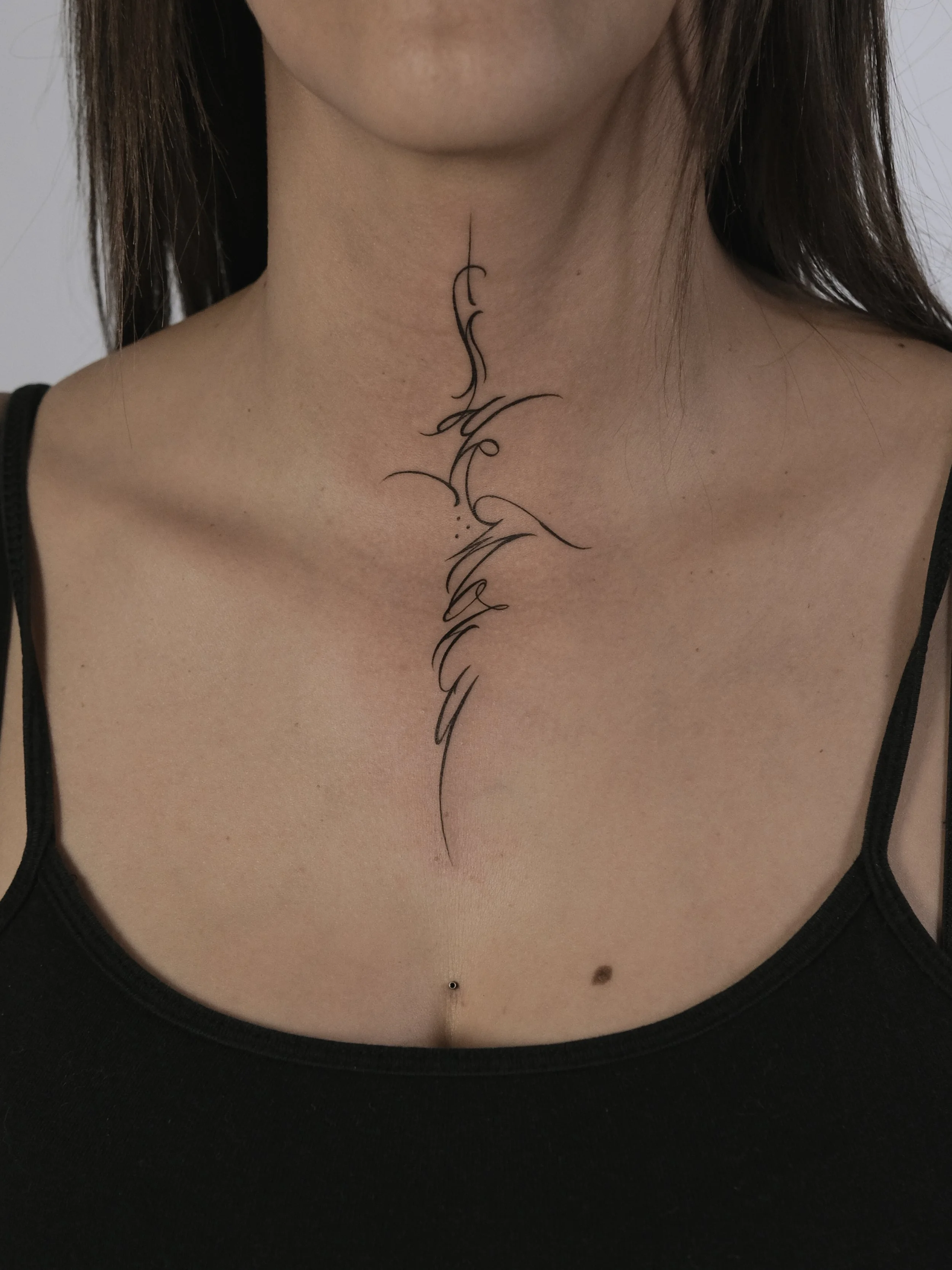 Person's neck tattoo with cursive script and thin lines.