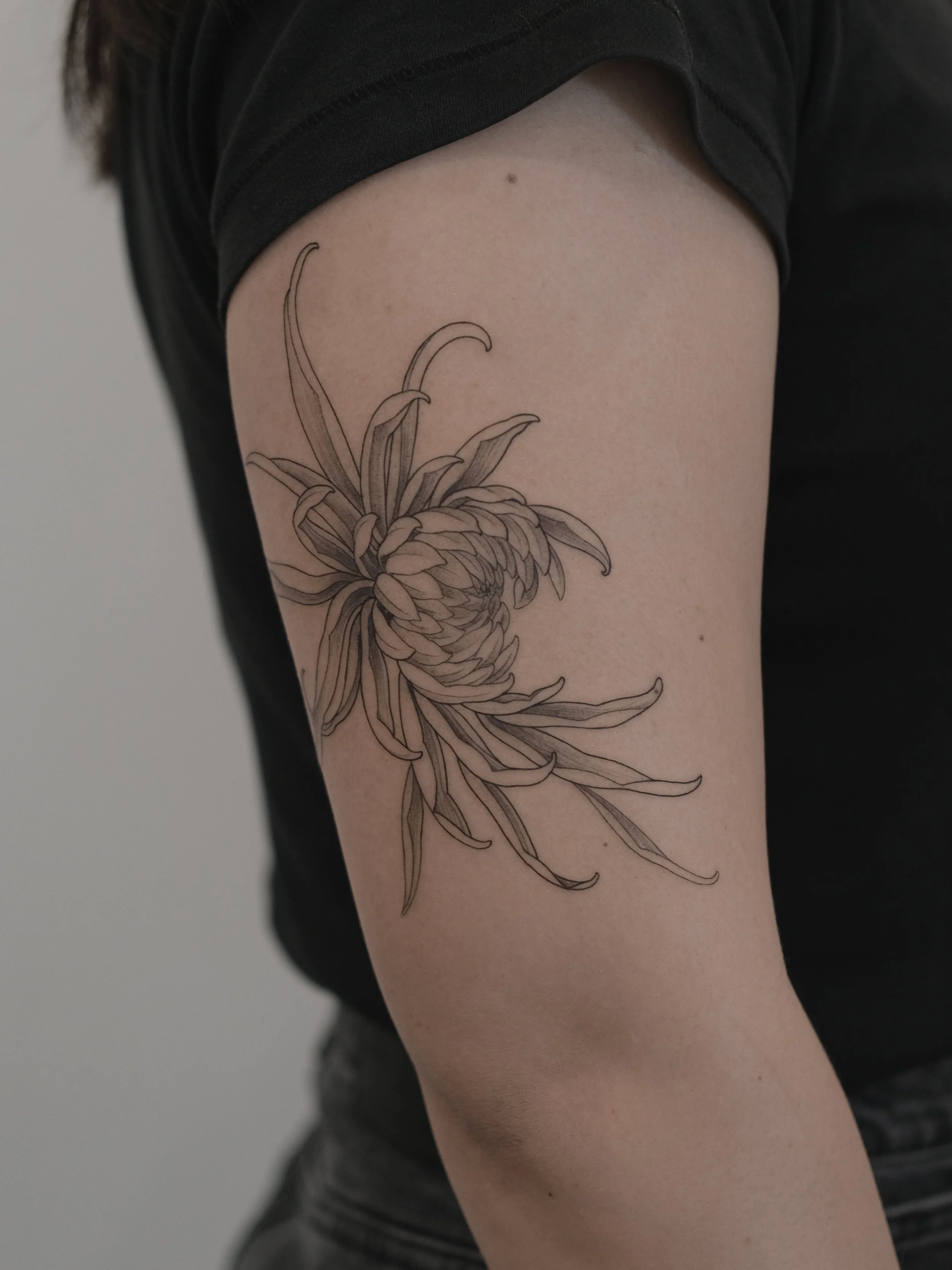 A person wearing a black shirt with a floral tattoo on their upper arm.