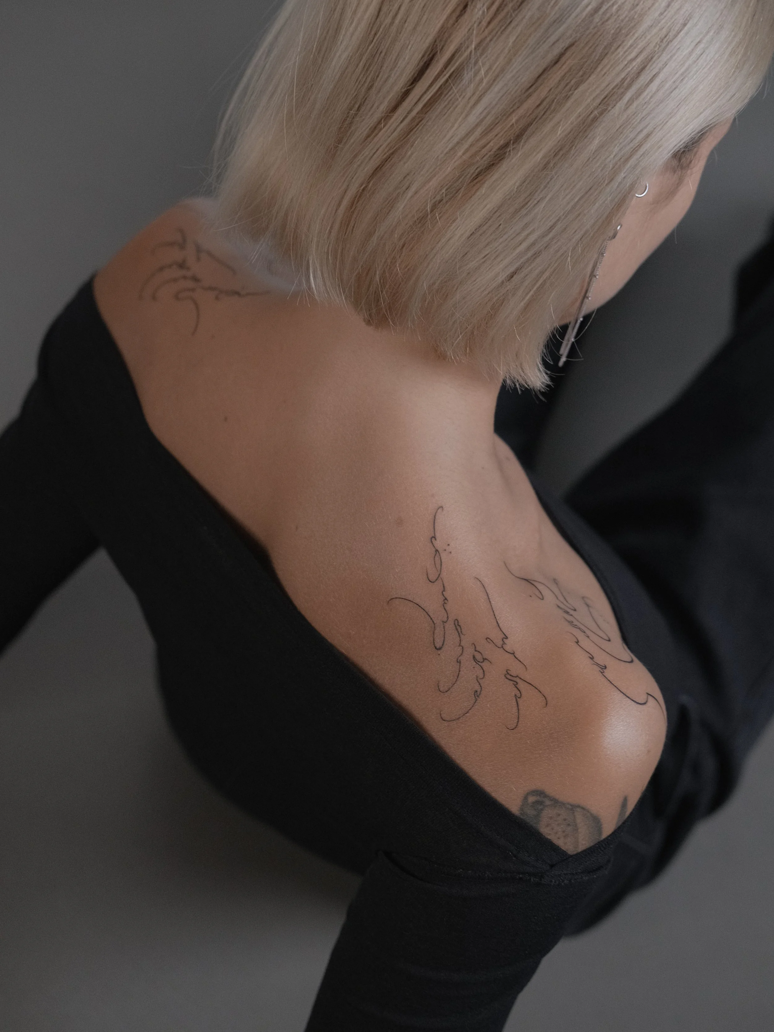Close-up of a woman's shoulder and upper chest, showing tattoos and blonde hair.
