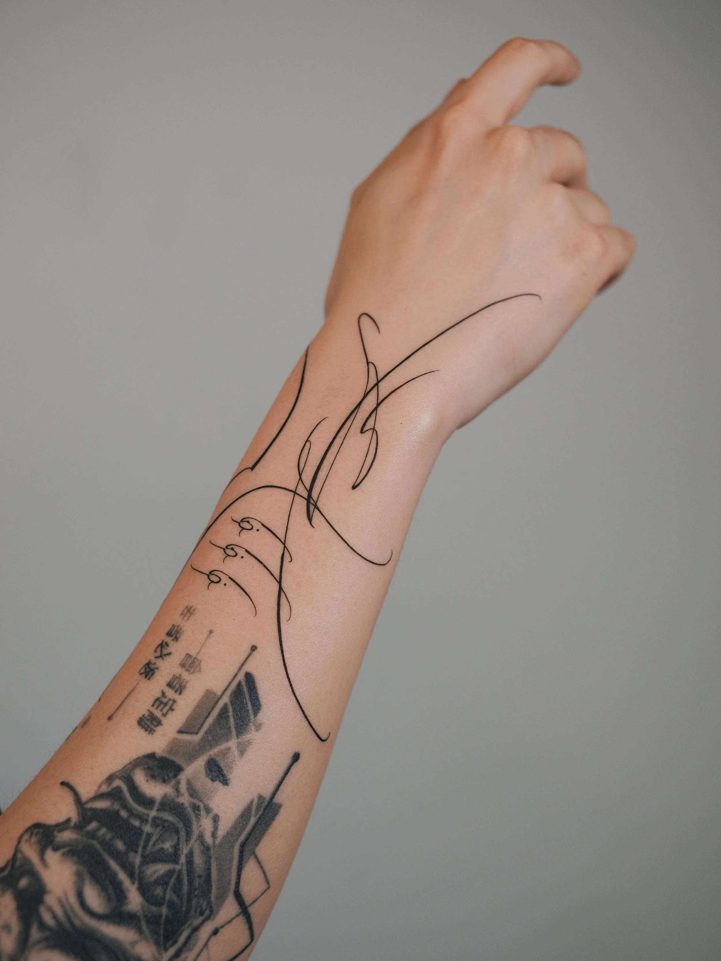 A person with tattoos on their arm and hand, showing black ink line art and Japanese characters, against a plain gray background.