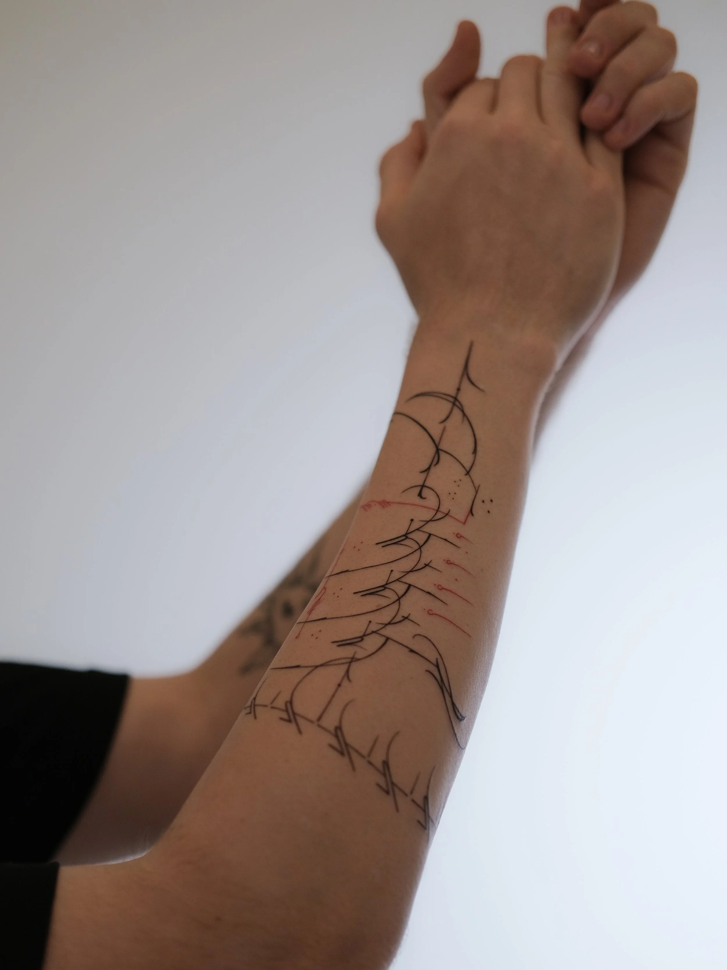 A person's arm with black ink tattoo lines in geometric and abstract styles.