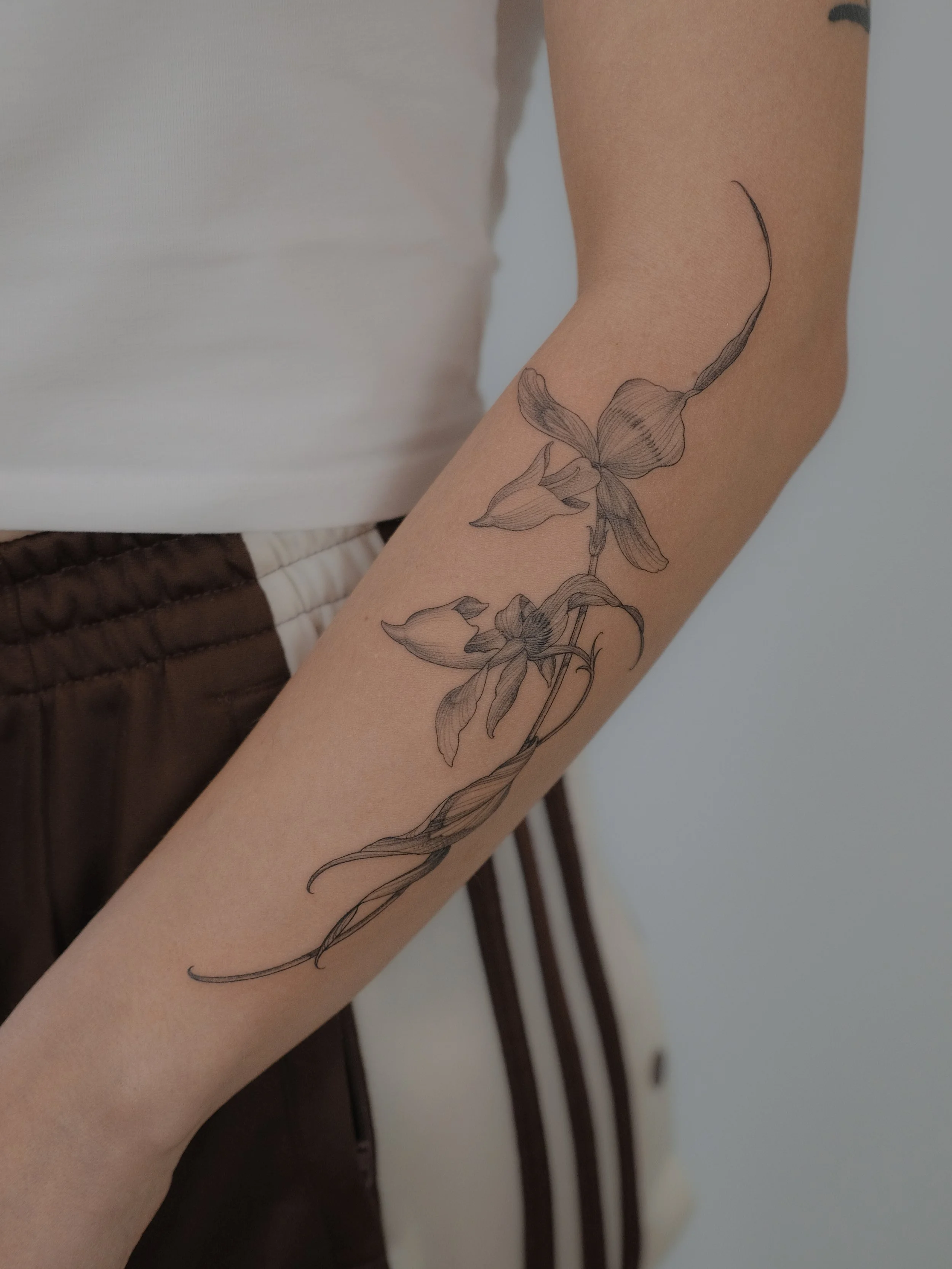 Close-up of a person's arm with a detailed black and gray floral tattoo of a flower and leaves.