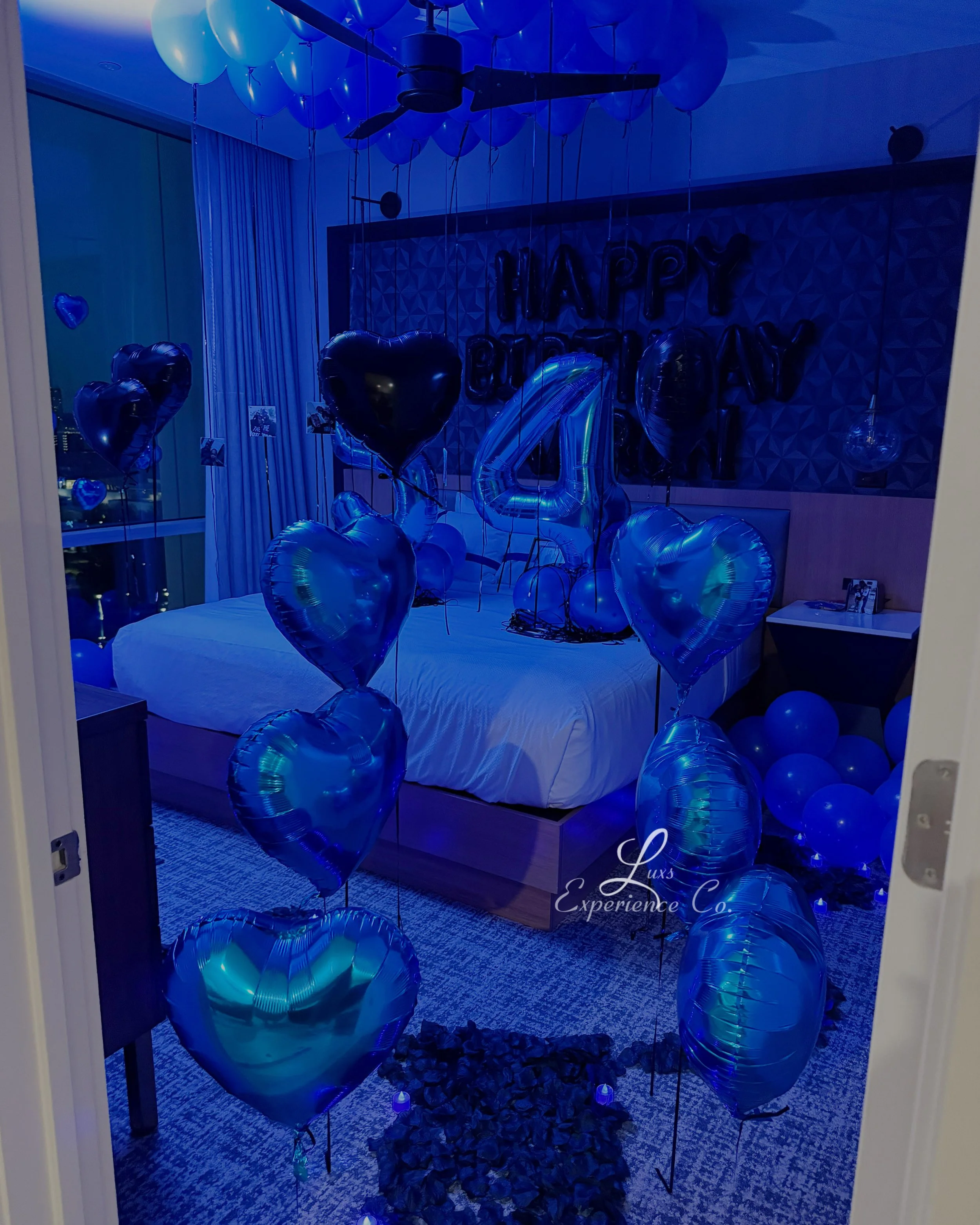 A bedroom decorated with blue balloons, including heart-shaped and number 