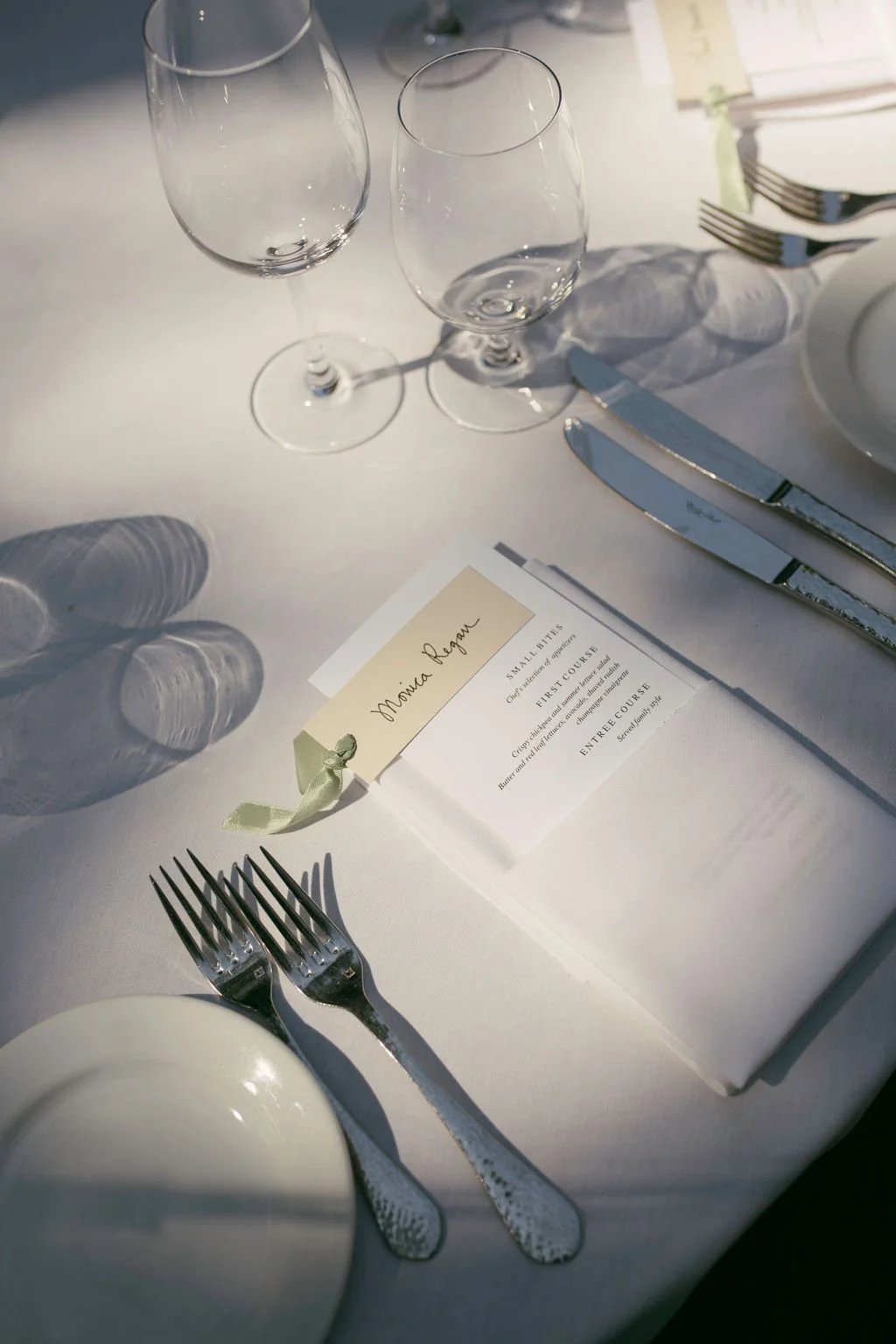 Elegant table setting with two empty wine glasses, a white plate, silverware, and a menu and place card with guest name.