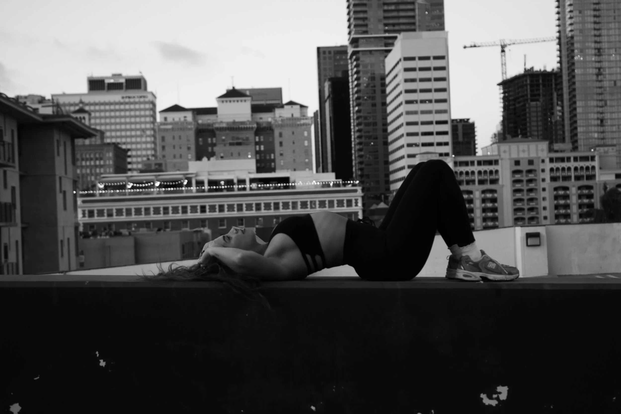 A woman lying on her back on a rooftop with city buildings in the background