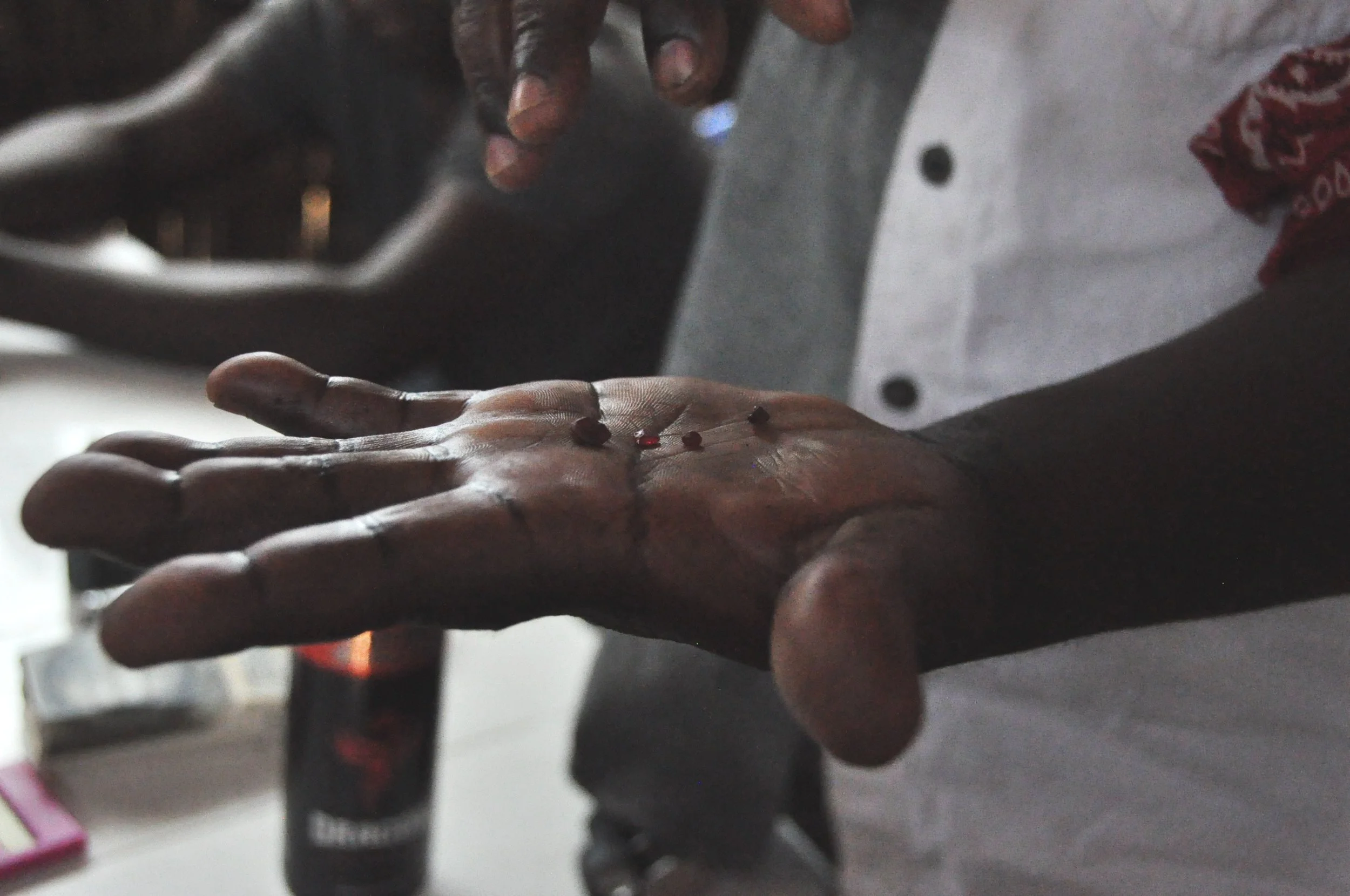 The hand of a gemstone miner, marked with dark substance and holding four rough red rubies in its palm
