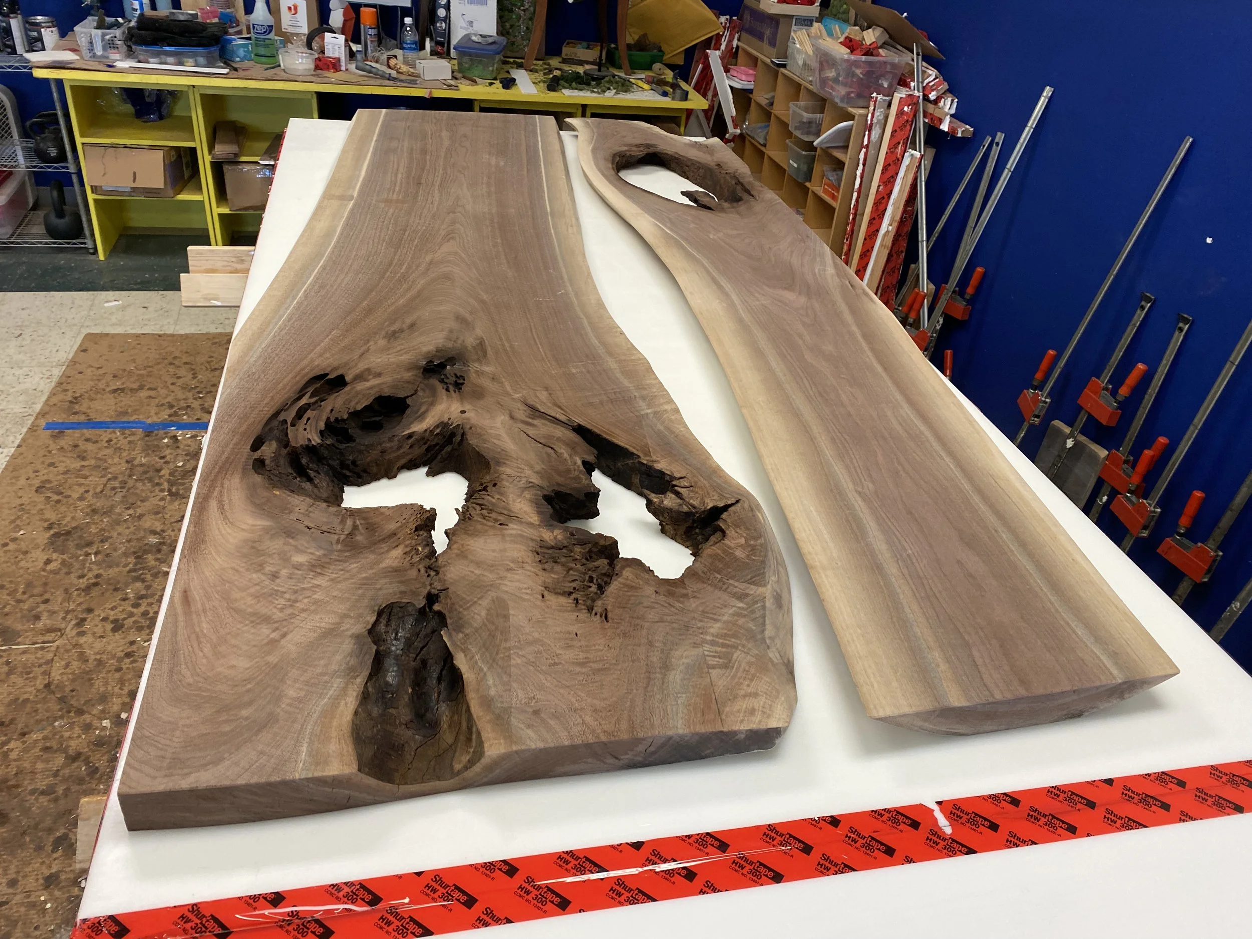 A large live-edge wooden slab with natural knots and grain, resting on a workbench in a woodworking shop.