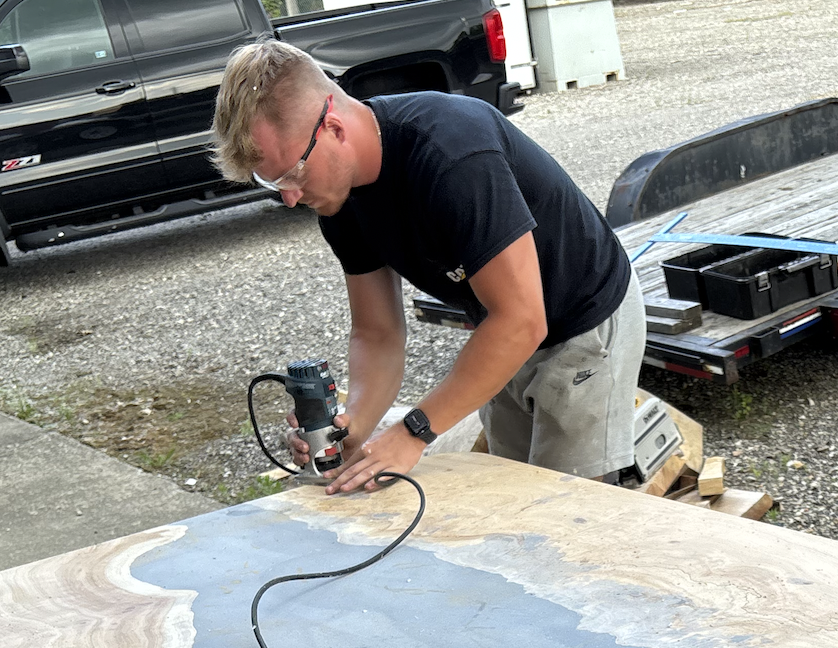 A man using a power sander on a wooden surface outdoors.