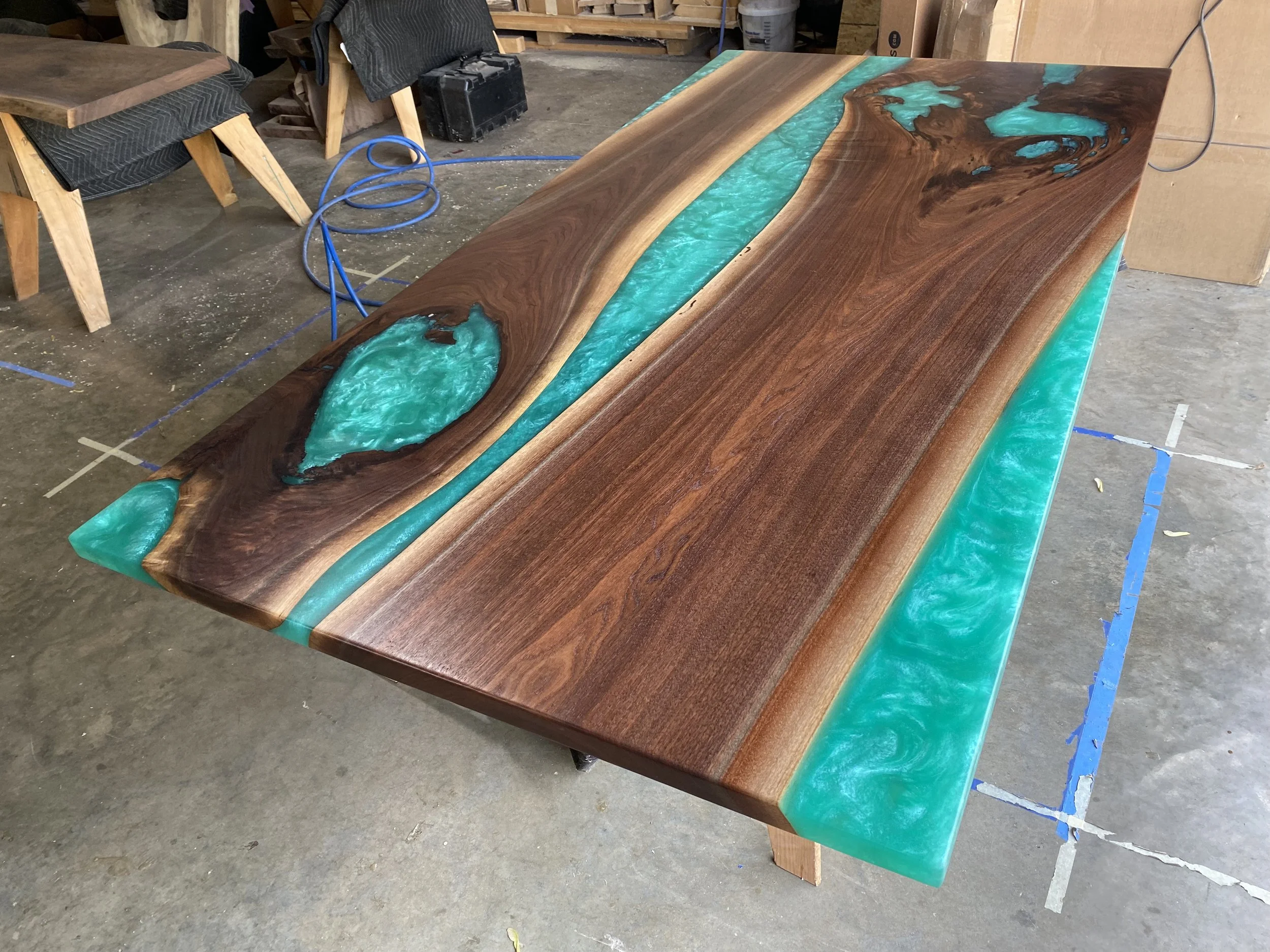 A wooden table with a natural wood finish and teal resin inlays, created in a woodworking shop.