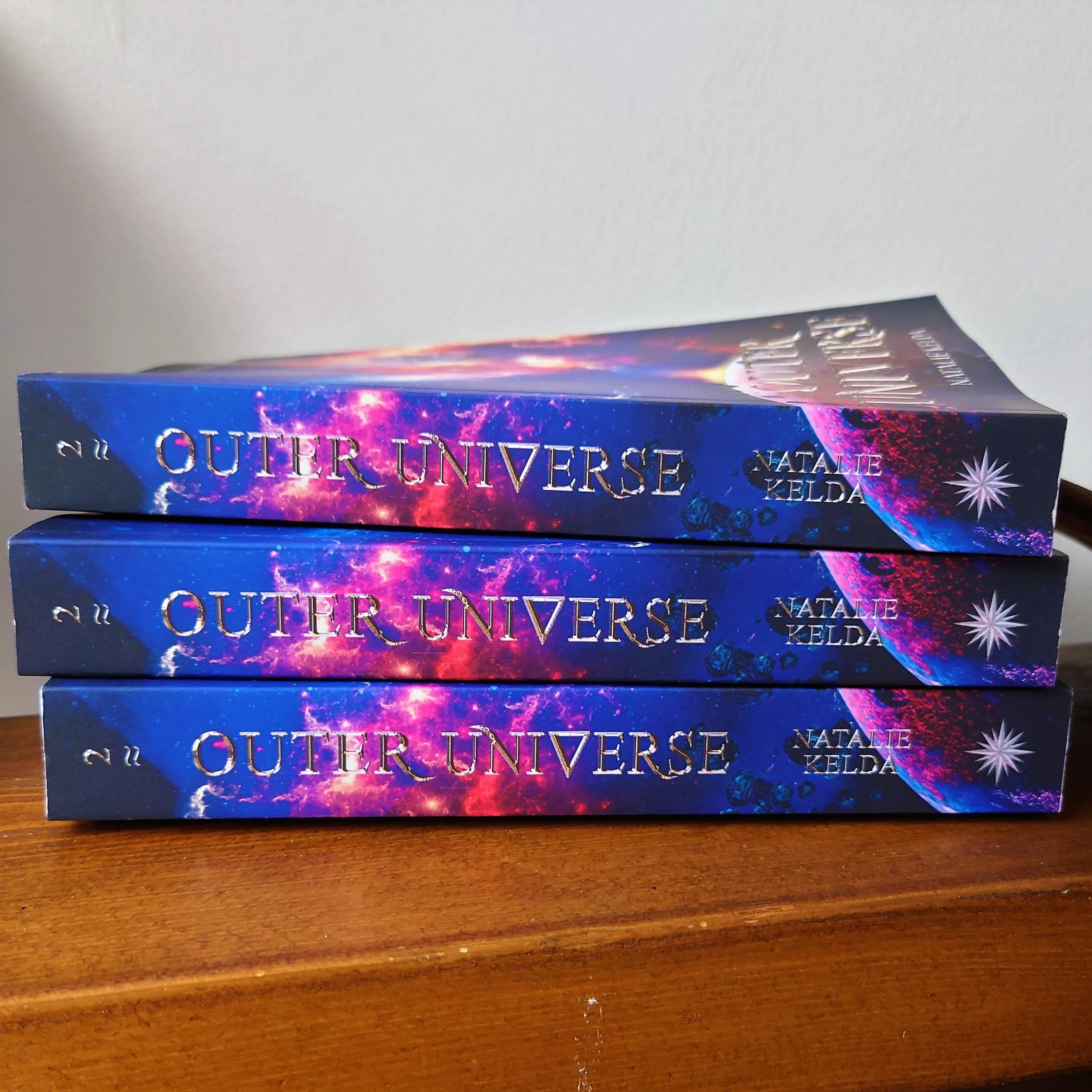 Three copies of Outer Universe lying on the side with the spine facing.