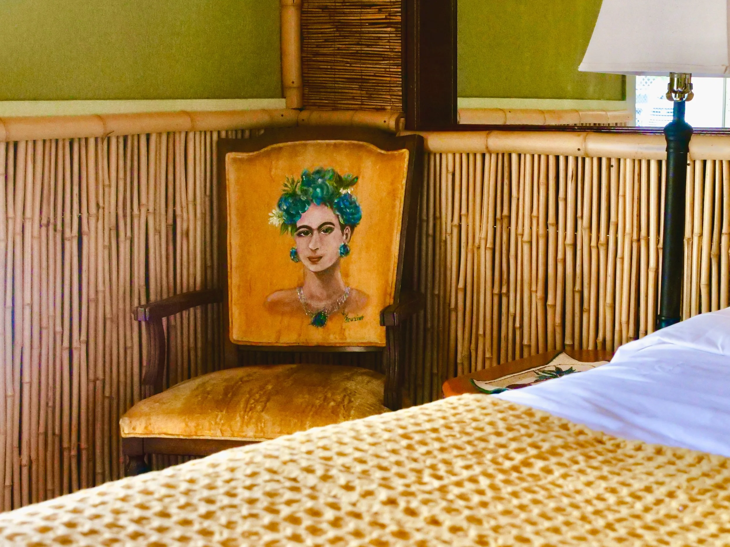 A chair with a painting of Frida Kahlo as the backrest in a tropical-themed room with bamboo decor.
