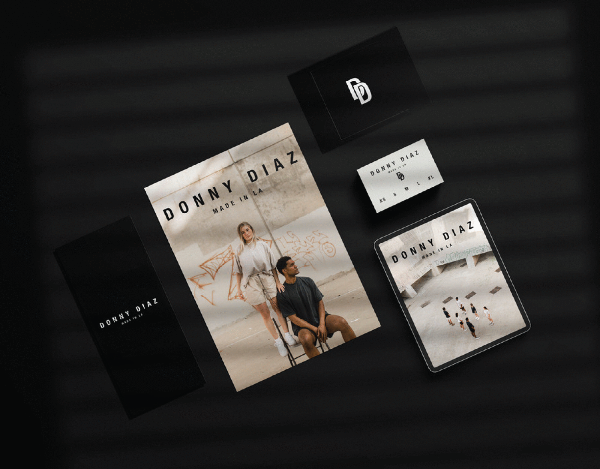 Promotional display for Donny Diaz featuring a poster of two models and a digital tablet showing the same poster, with the overall scene set against a black background.