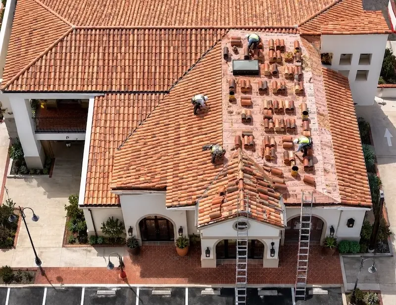Roofing crew working on a commercial tile re-roofing project, showing underlayment and stacked tiles.
