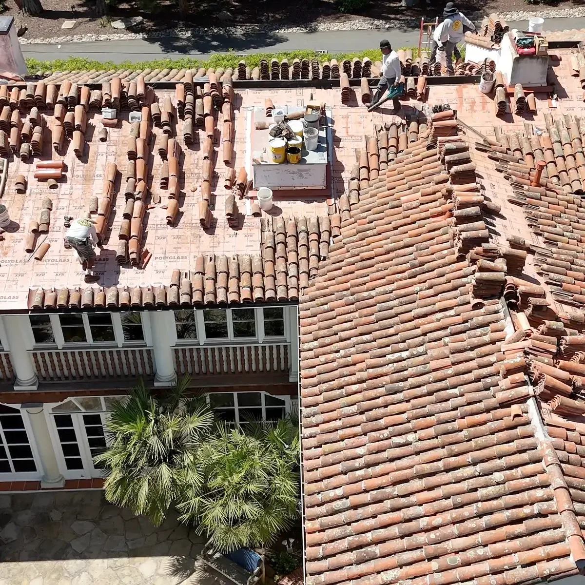 Roofers working on a steep-pitched residential roof, installing new underlayment and materials.