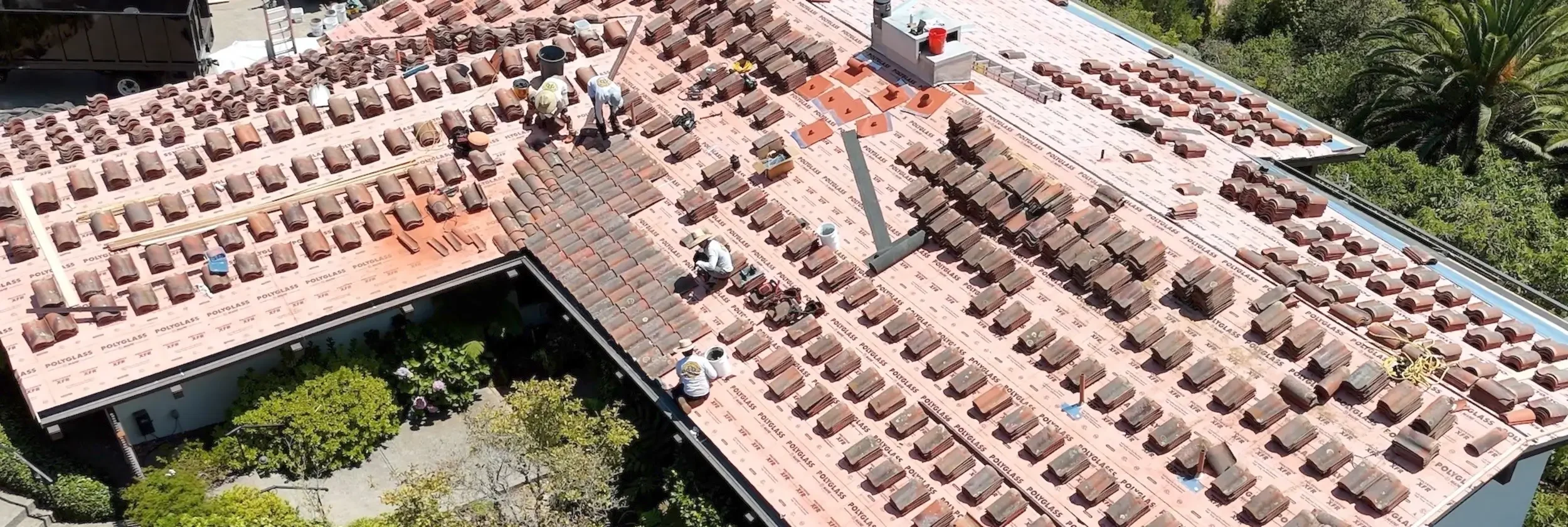 Roof replacement in Santa Barbara with a crew installing clay tile roofing and underlayment on a residential home.