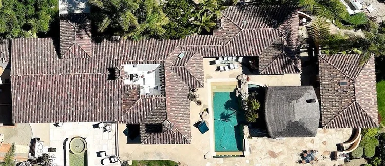Drone view straight down on a luxury Santa Barbara estate with a multi‑level mission clay tile roof surrounding a central pool courtyard.