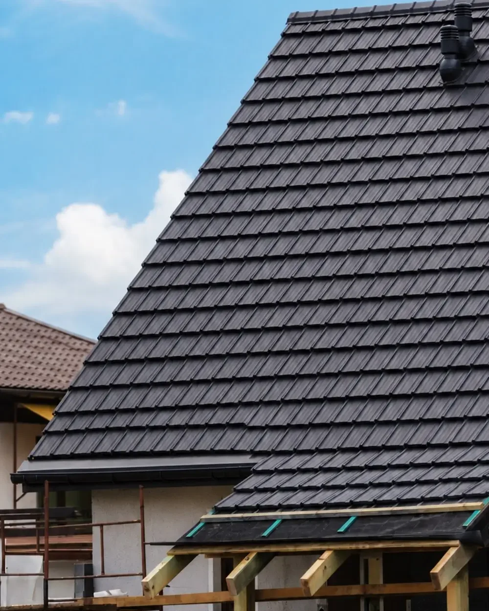 Close-up of newly installed dark synthetic slate roofing tiles showing the overlapping installation process.