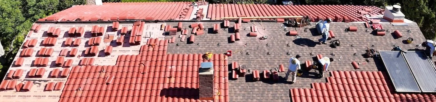 Roofing crew installing new red clay tiles during a residential reroofing project