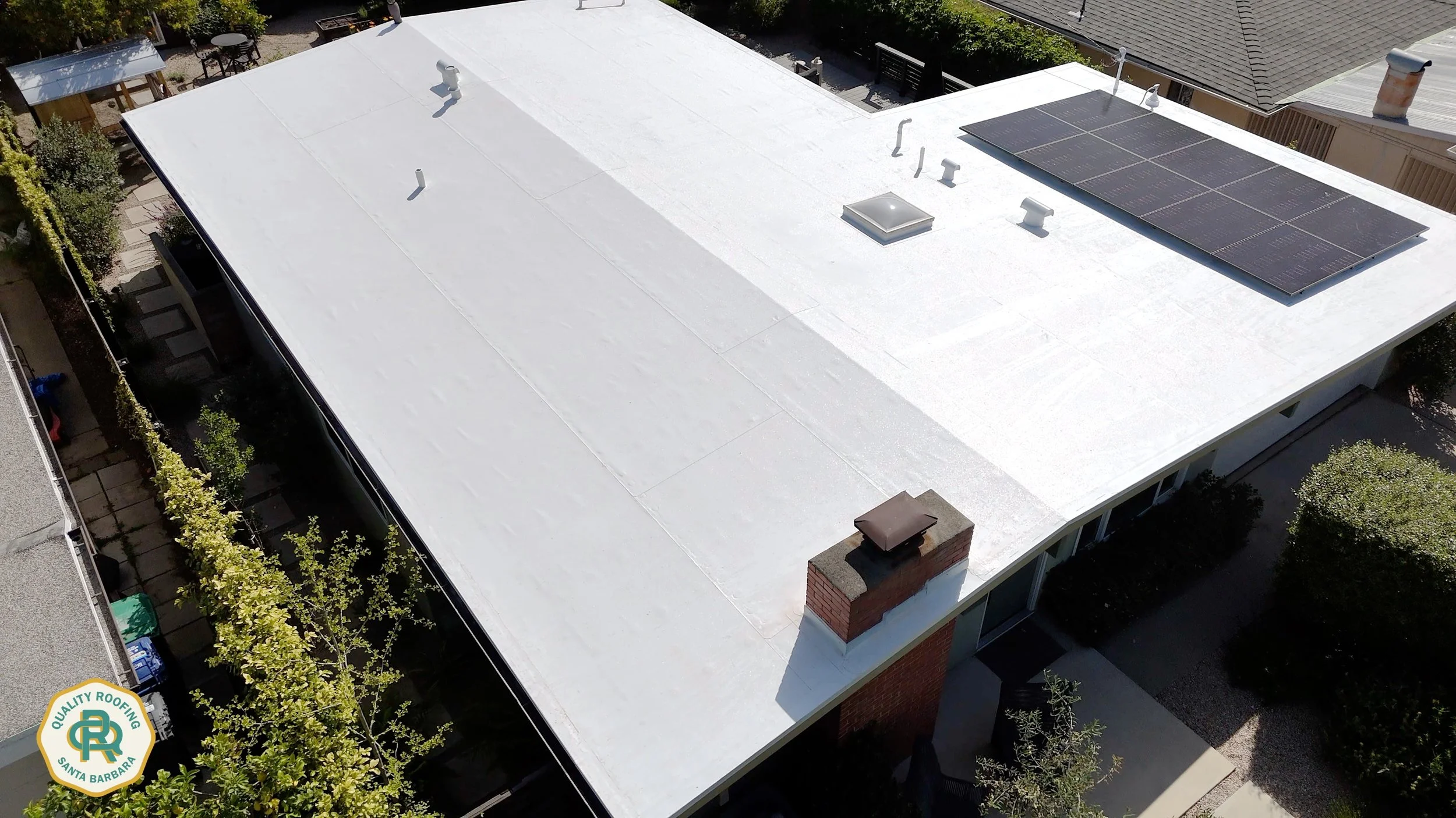 Drone view of a white PVC flat roof with integrated solar panels on a modern home in Santa Barbara, California.