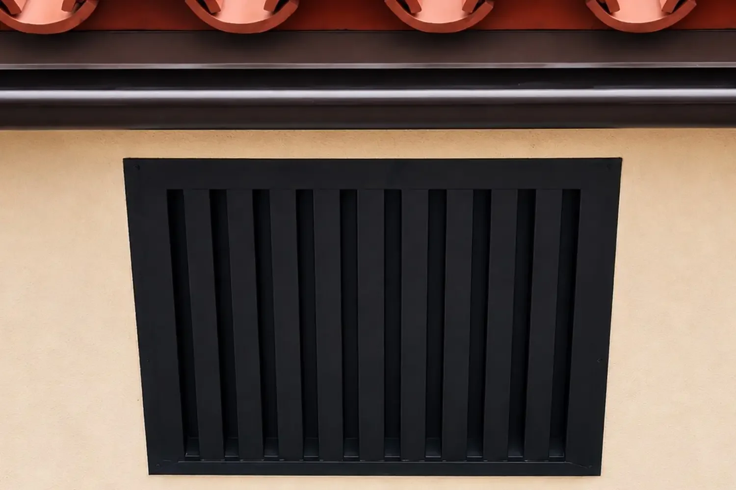 Black ember-resistant eave vent installed under a red clay tile roof.