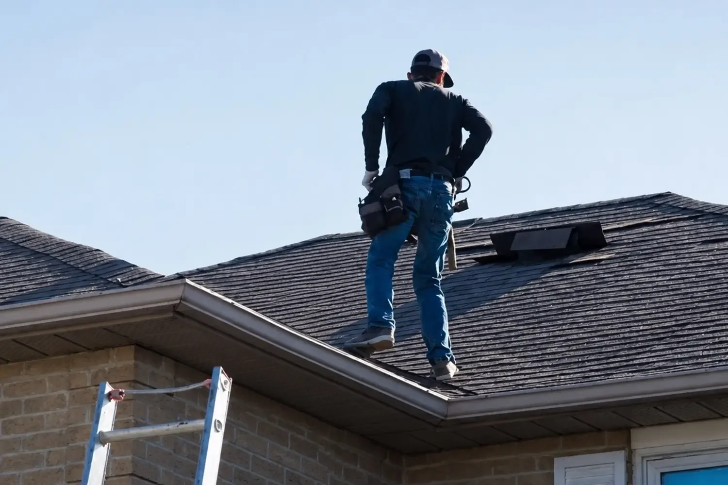 Roofer on a ladder performing a safety inspection on a shingle roof.