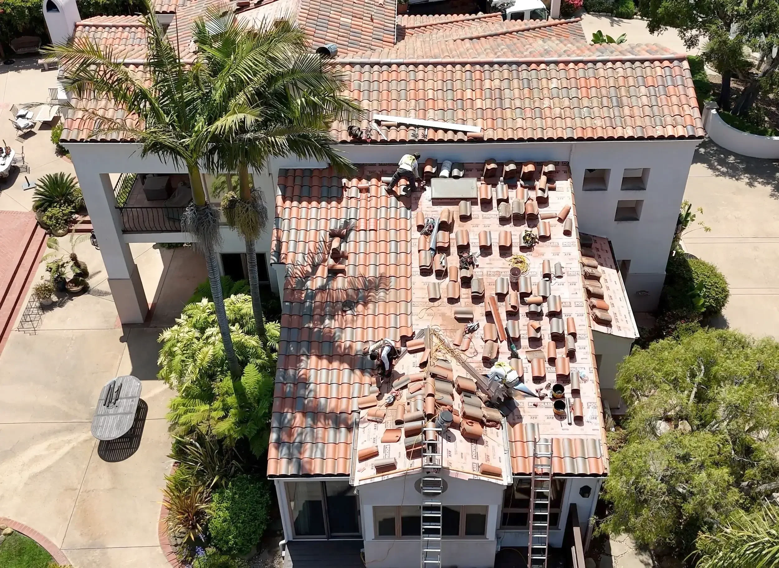Aerial view of a roofing crew performing a partial reroof on a residential red clay tile roof.