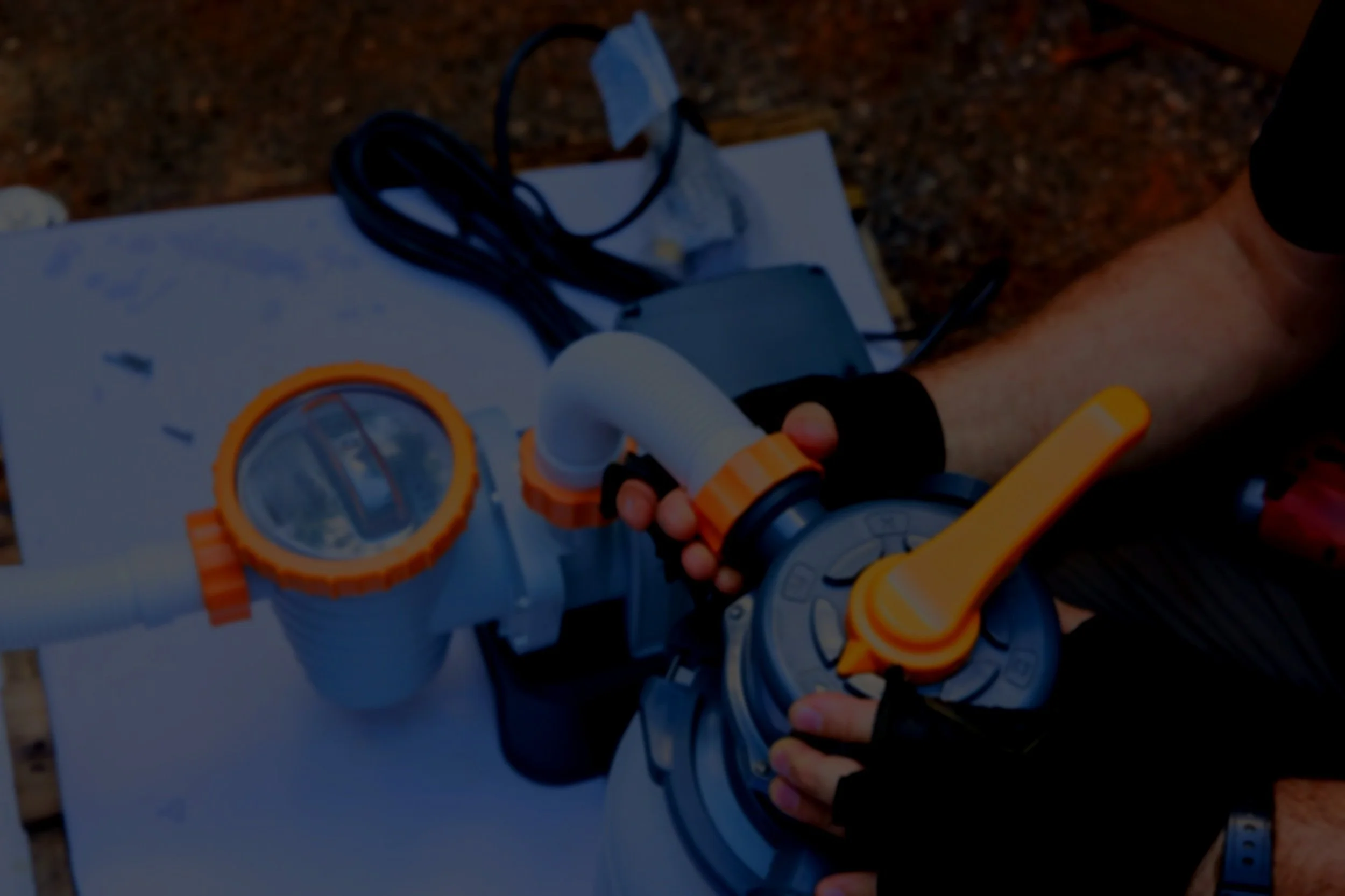 A person holding a toy blaster with black and orange details, pointed towards the right, with a background of a white flat surface and blurred outdoor ground.