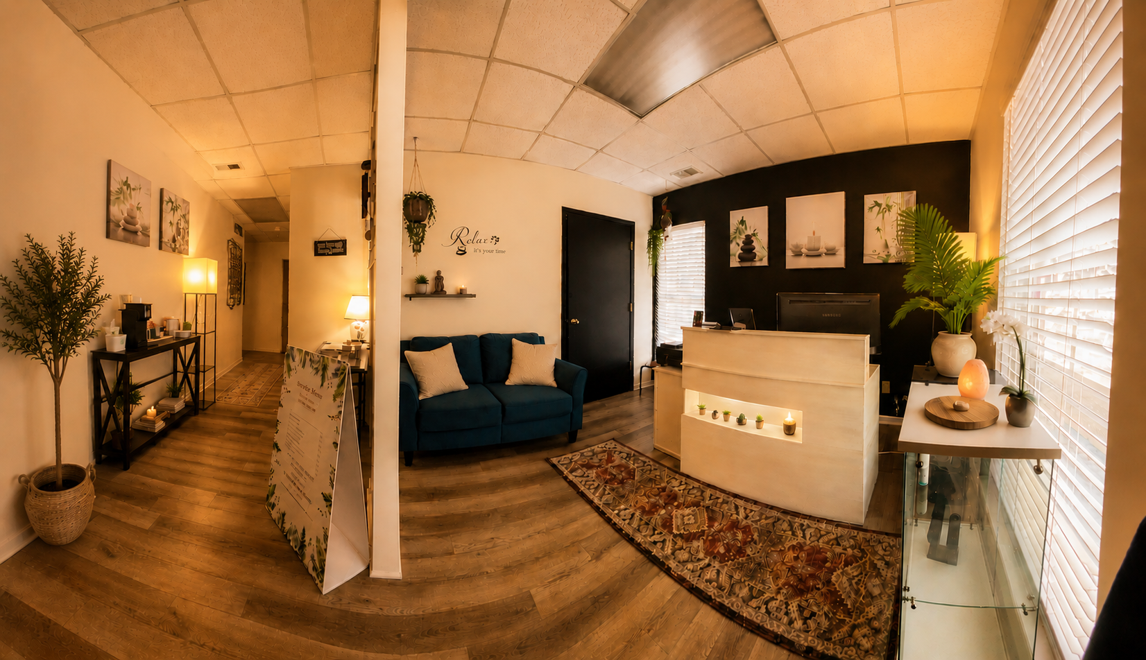 Interior of a wellness or spa reception area with a cozy seating area, decorative plants, wall art, and warm lighting.