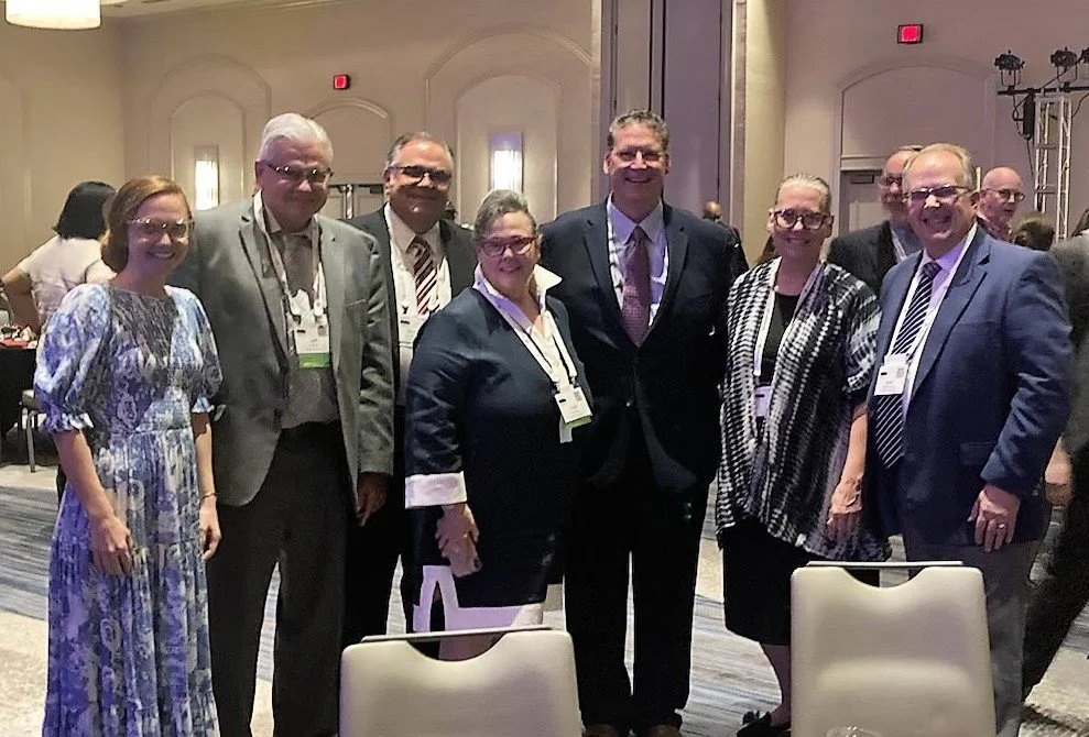 Group of seven people standing together at an indoor conference or event, smiling at the camera.