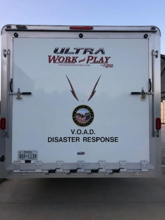 Back of a white emergency response trailer with logos and text, including 'ULTRA WORK and PLAY,' 'V.O.A.D. DISASTER RESPONSE,' and the Texas license plate B04-1139.