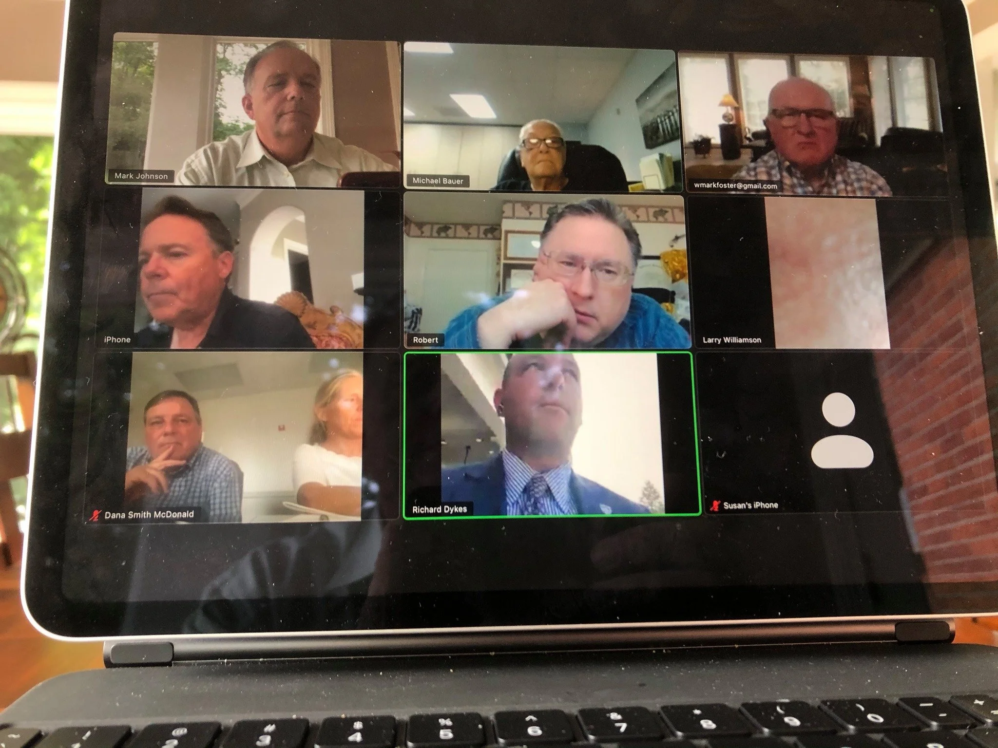 A screenshot of a virtual video conference with eight participants, including a mix of men and women, some with glasses, with relaxed or attentive expressions, displayed on a laptop screen.