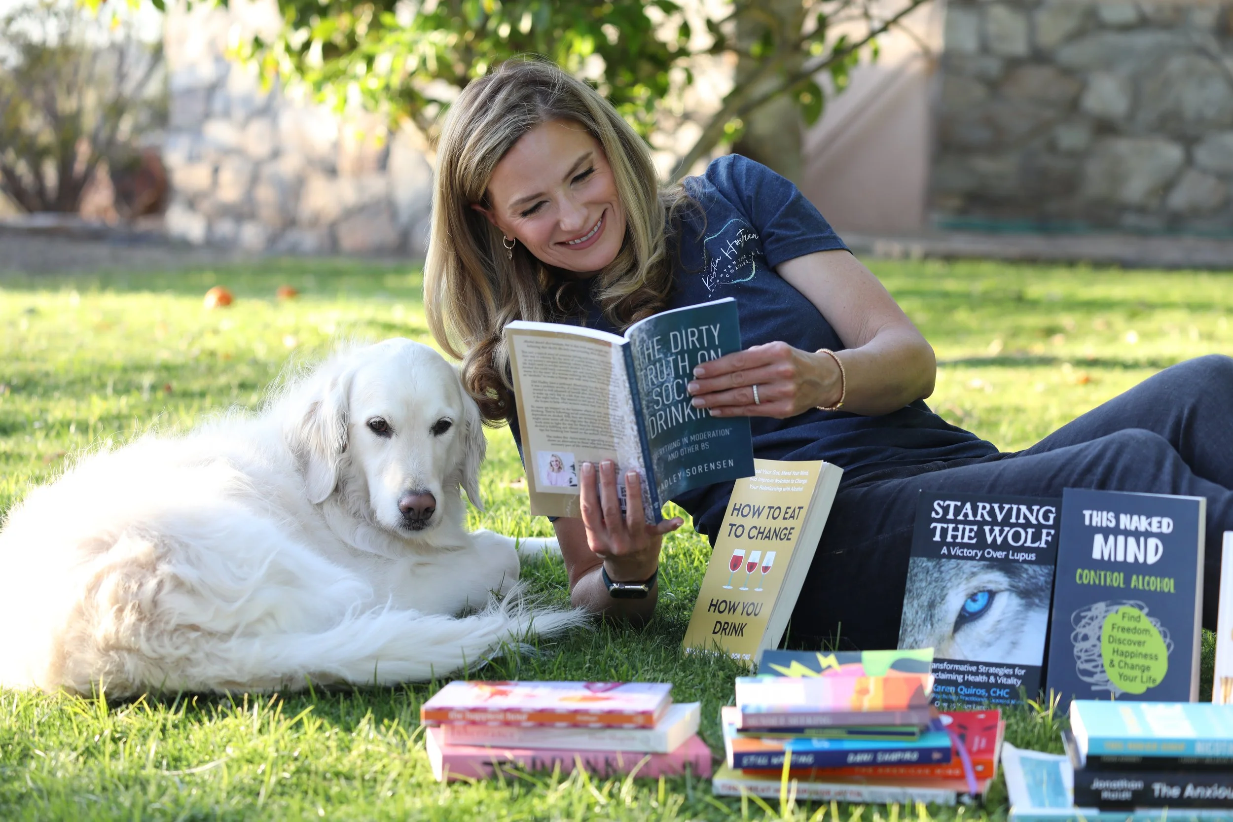 Gray area drinking coach Kristin Horstman reading sobriety and wellness books outdoors with her dog Aurora