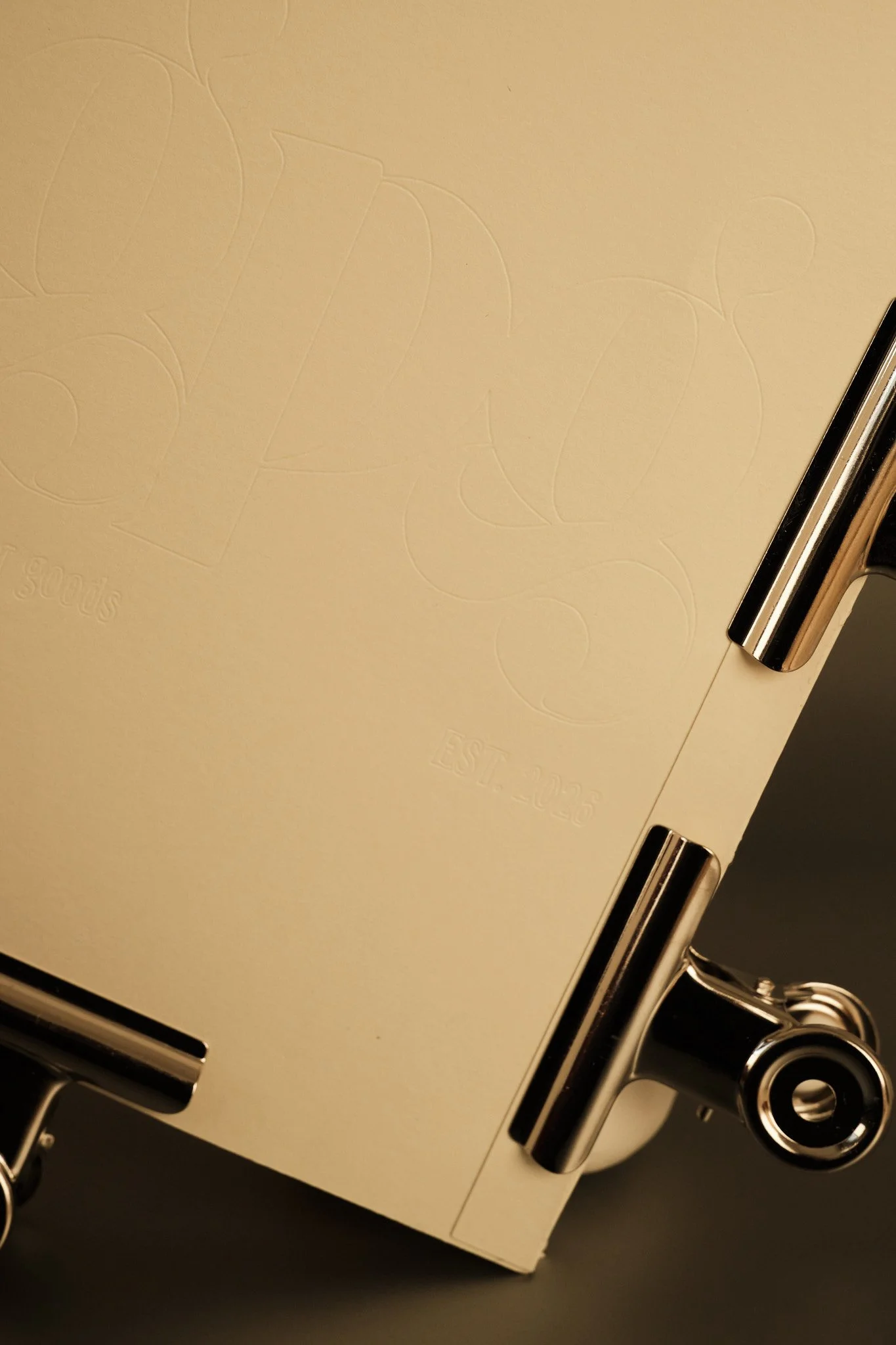 Close-up of a beige metal box with embossed lettering, featuring metallic hinges and a matching metal handle, against a dark background.